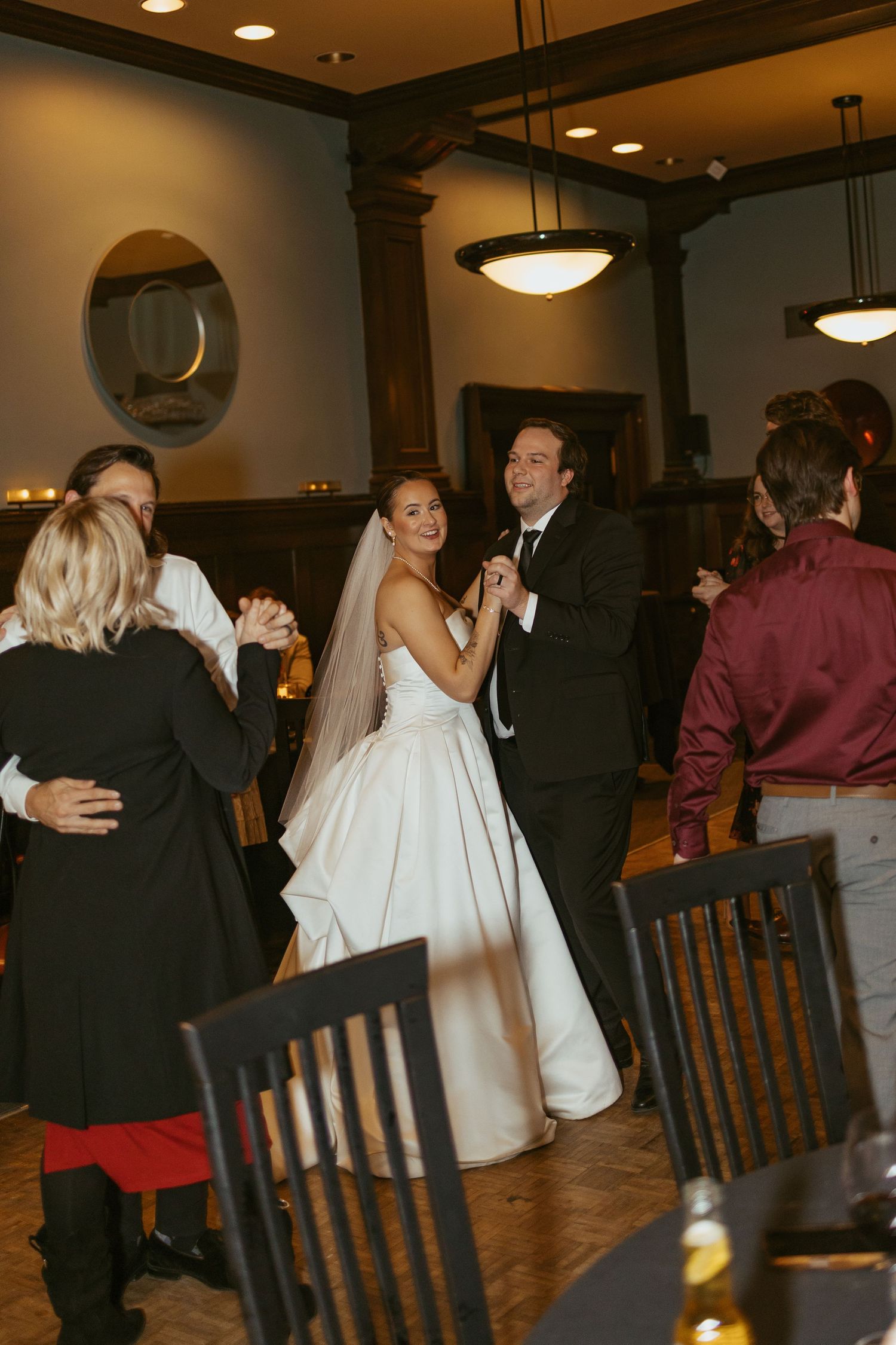 Wedding reception dance floor scene with guests celebrating in an elegant venue with pendant lighting.