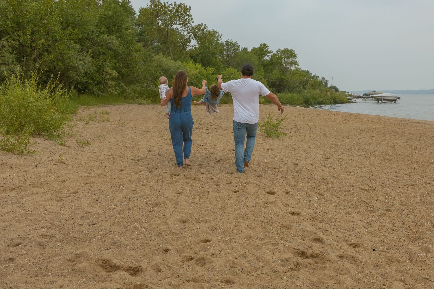 People walking along a sandy beach path surrounded by greenery near the water.