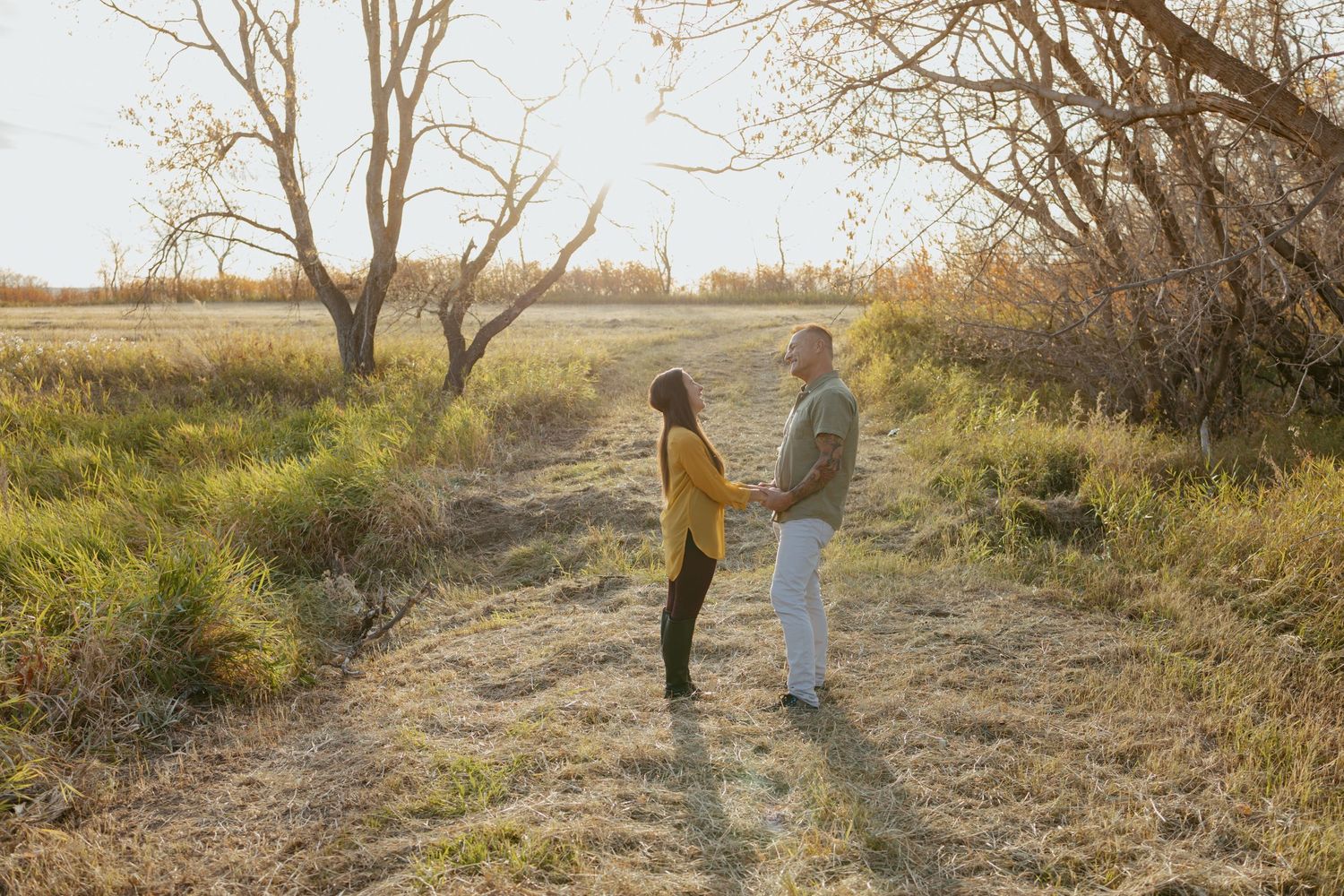 Silhouettes of two people walking through a grassy field at sunset.