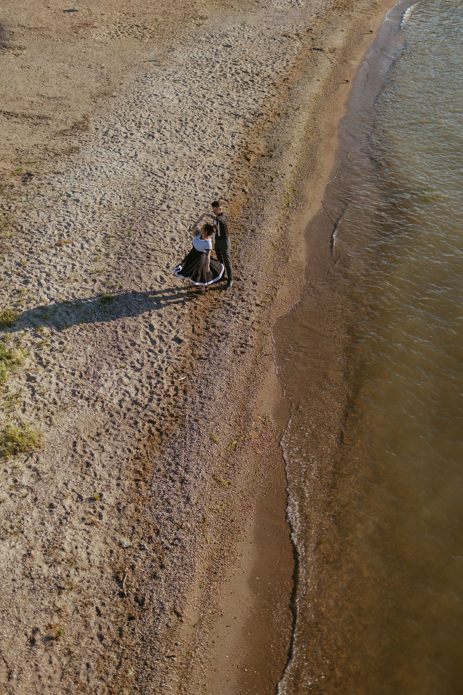 Aerial view of a couple standing on a rocky beach shoreline.