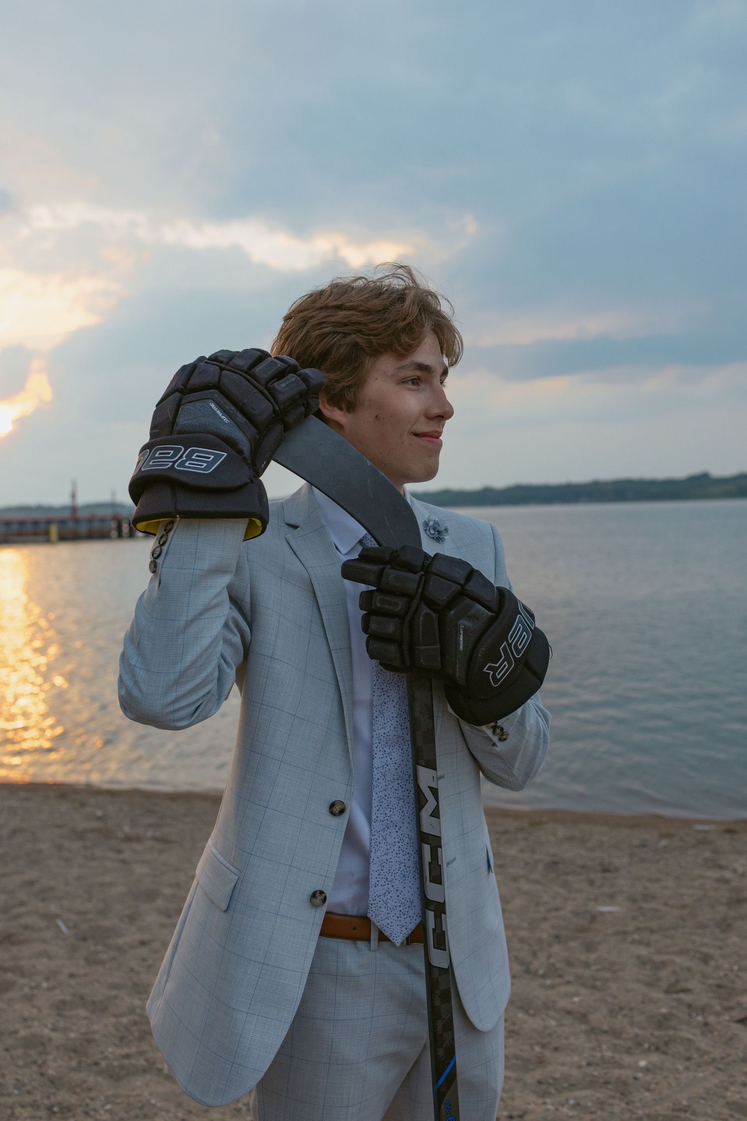 Someone wearing a light blazer poses dramatically on a beach at dusk with water in the background.