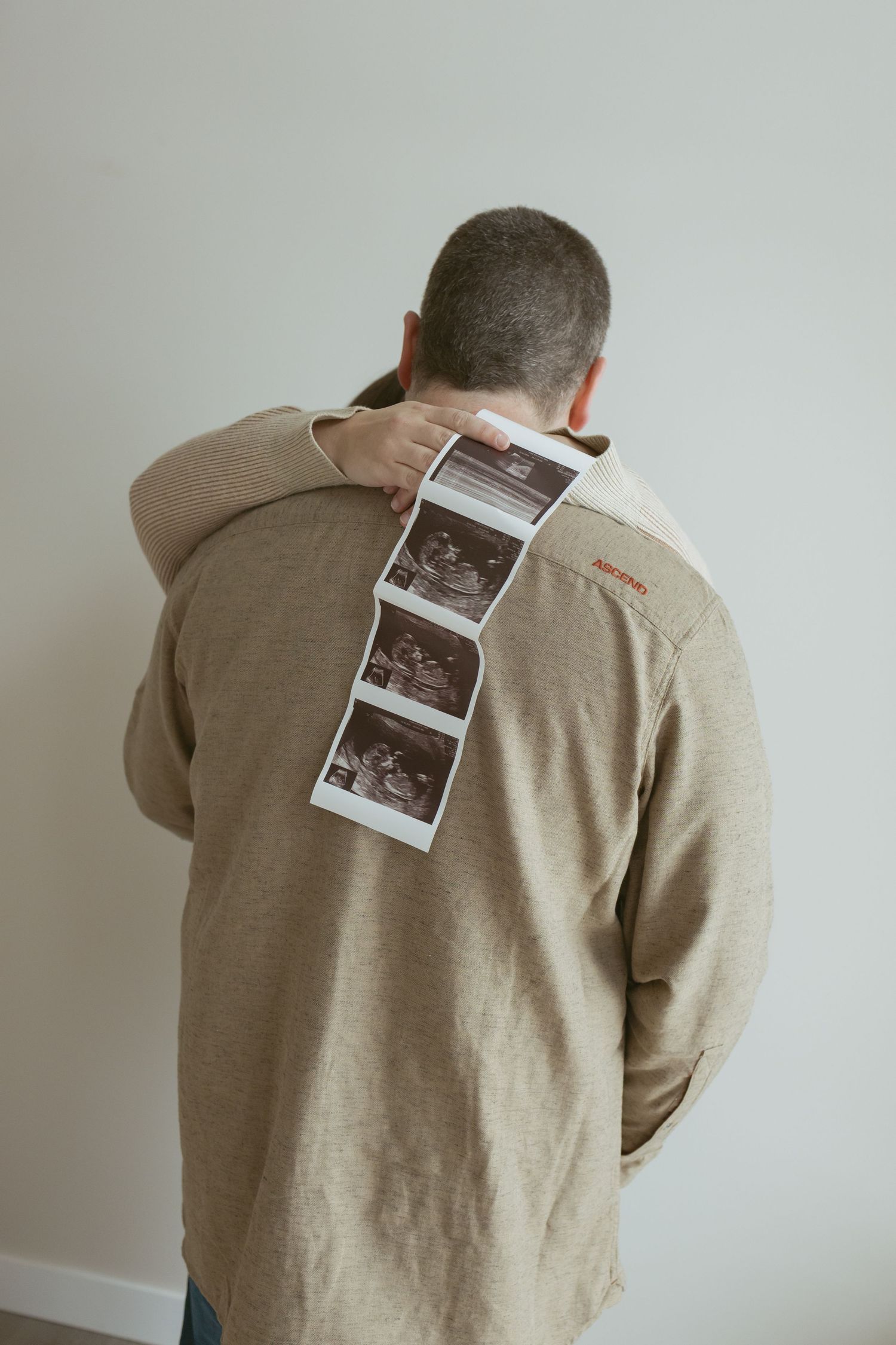 Man holding ultrasound photos behind his back, wearing a beige jacket, pregnancy announcement concept.