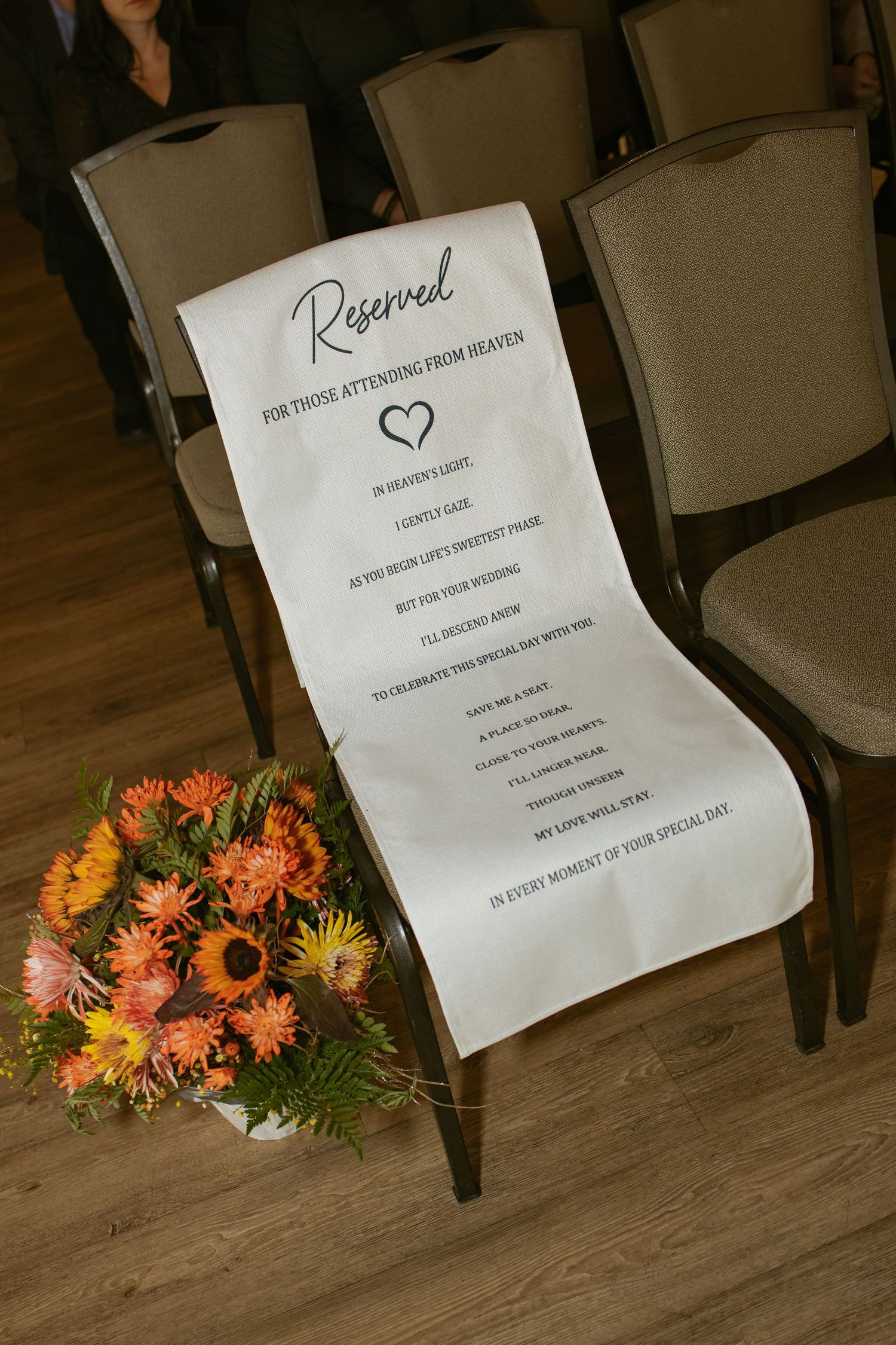 Reserved wedding chair sign for loved ones in heaven, with orange floral arrangement at a ceremony venue.