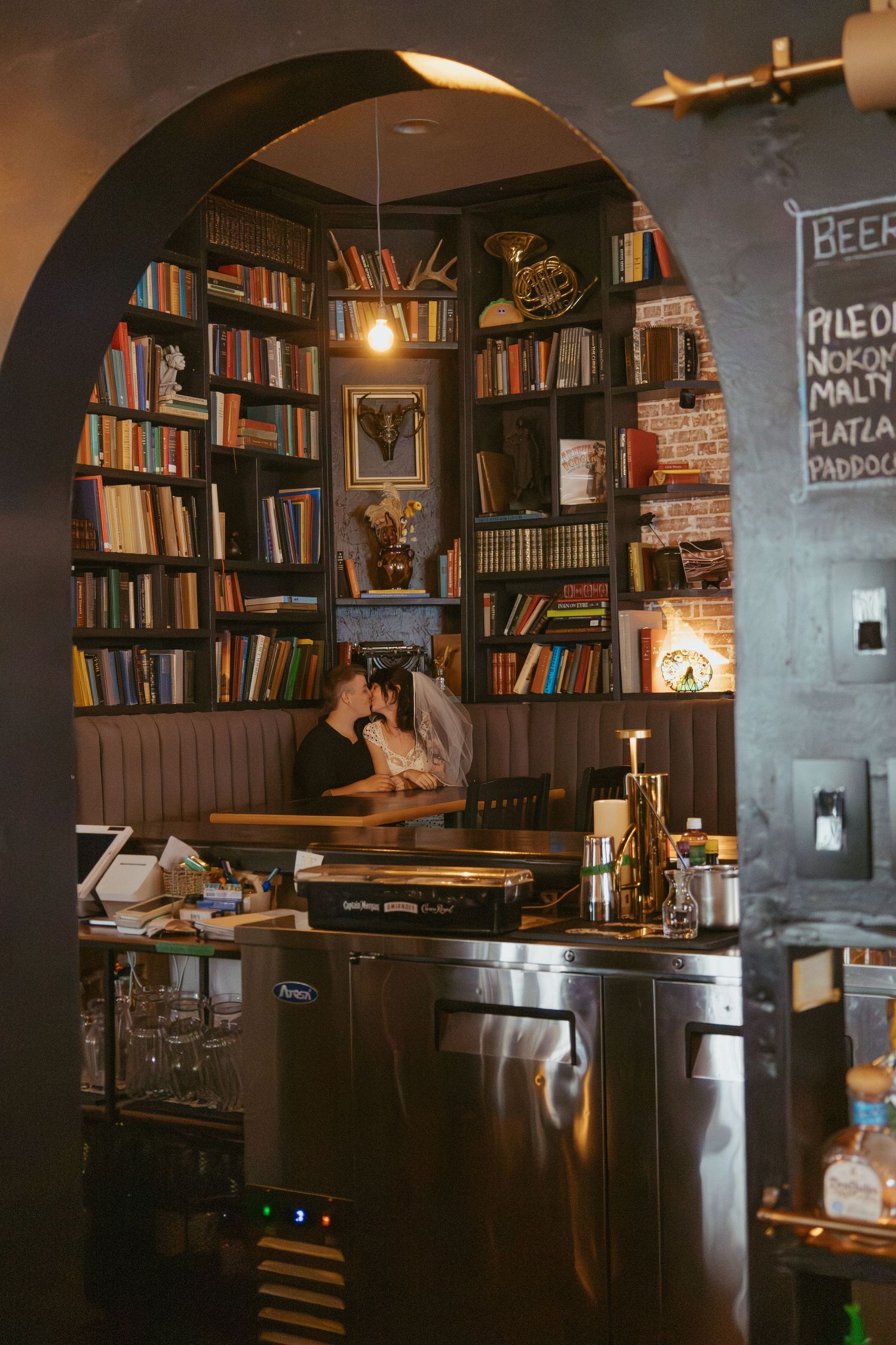 A cozy bar interior with wooden arches, bookshelves, and ambient lighting.