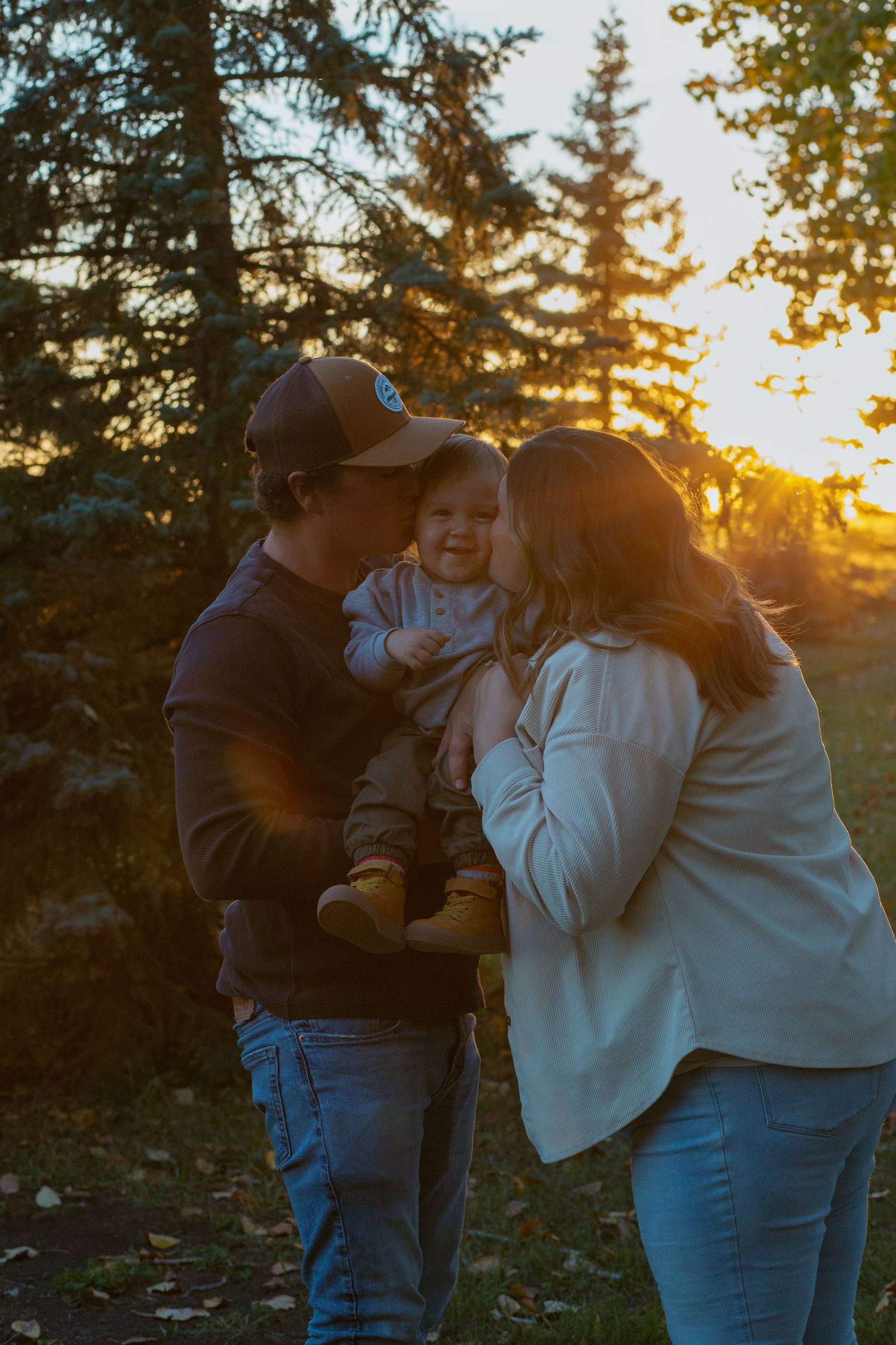 Silhouettes of people embracing at sunset with evergreen trees in the background.