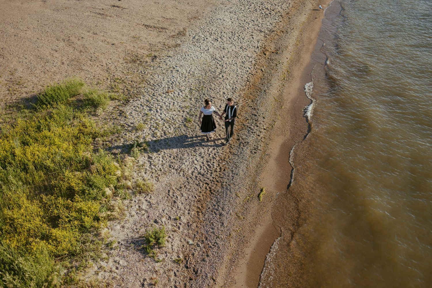 Aerial view of a couple walking along a beach shoreline with dramatic shadows.