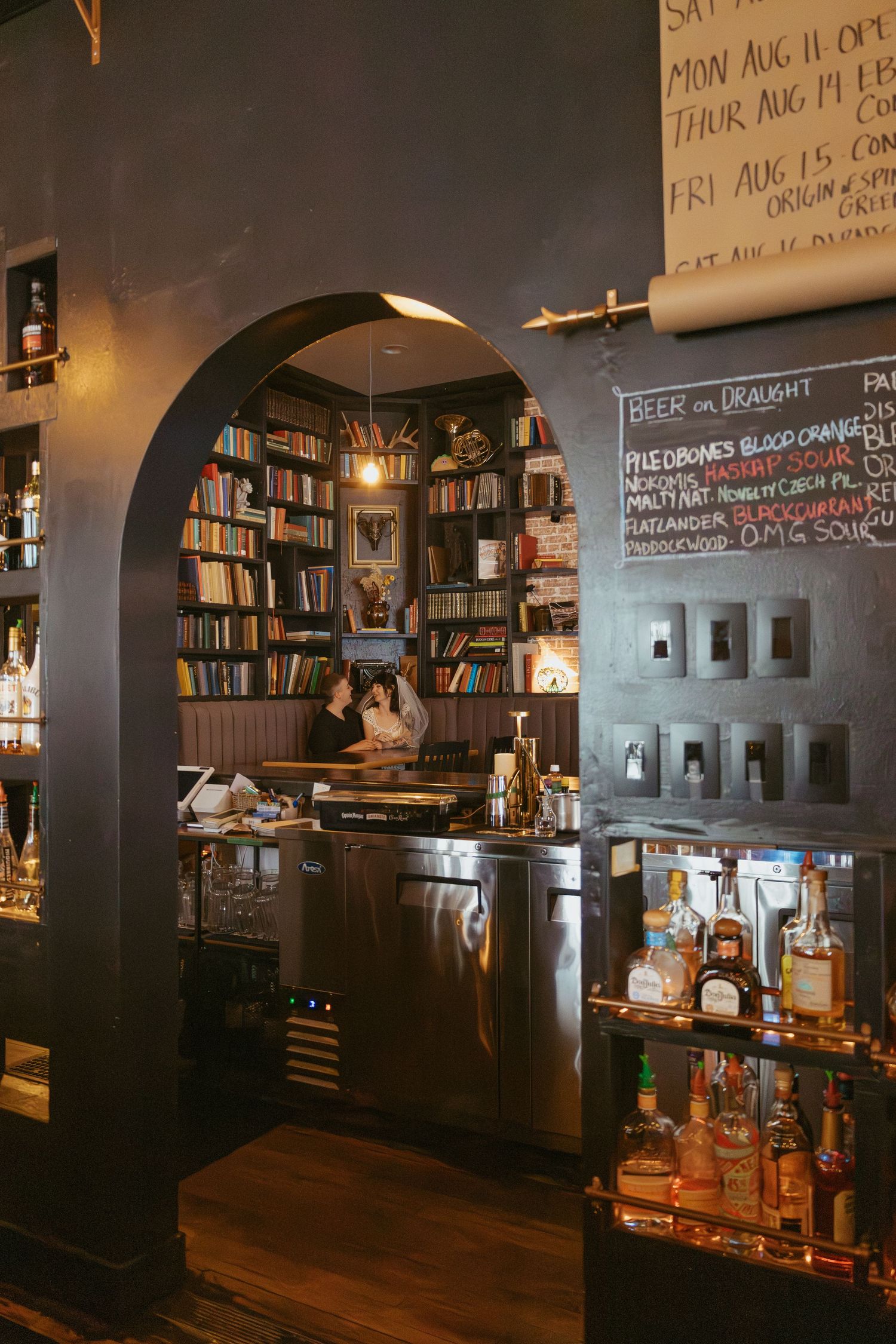Dark interior of a bar or cafe with arched doorways and bookshelves.