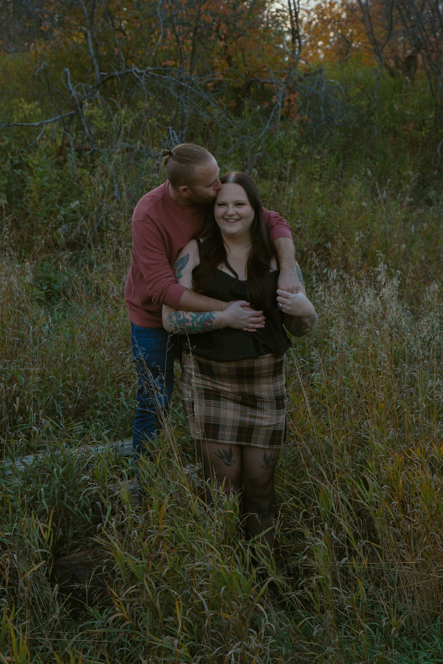 A couple shares an intimate moment among tall grass and autumn trees.