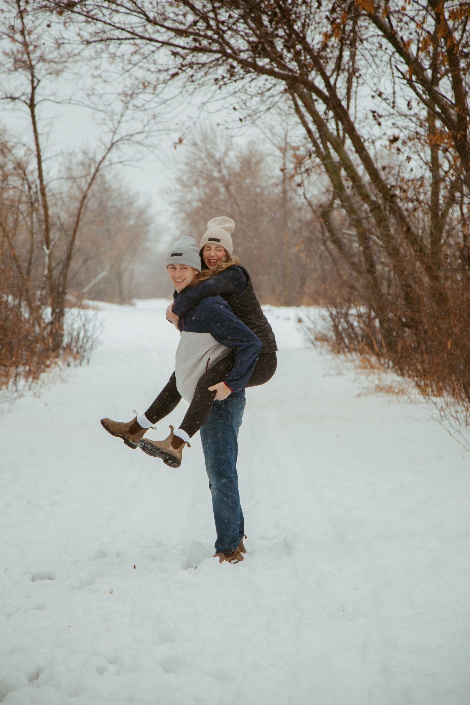 Playful winter moment captured as one person lifts another in a snowy forest setting.