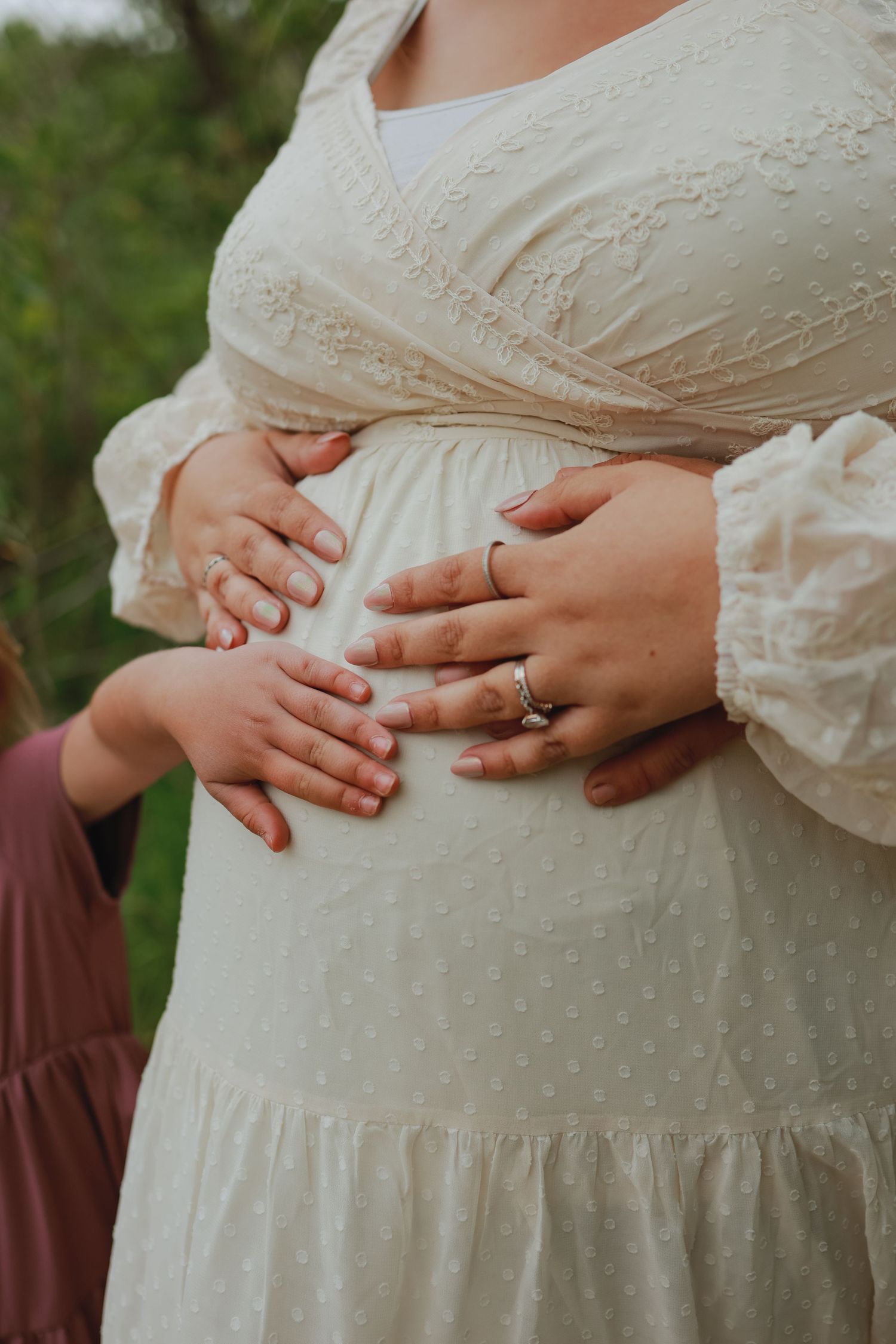 Close-up of hands resting on a white lace maternity dress showing wedding ring.