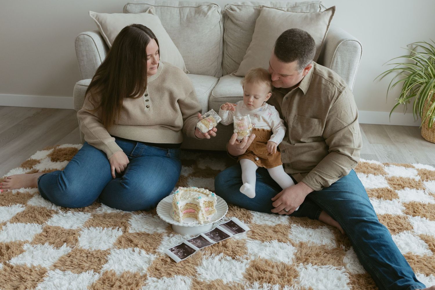 Family sitting on a cozy rug with their baby, ultrasound photos nearby, sharing a tender moment by a beige sofa.