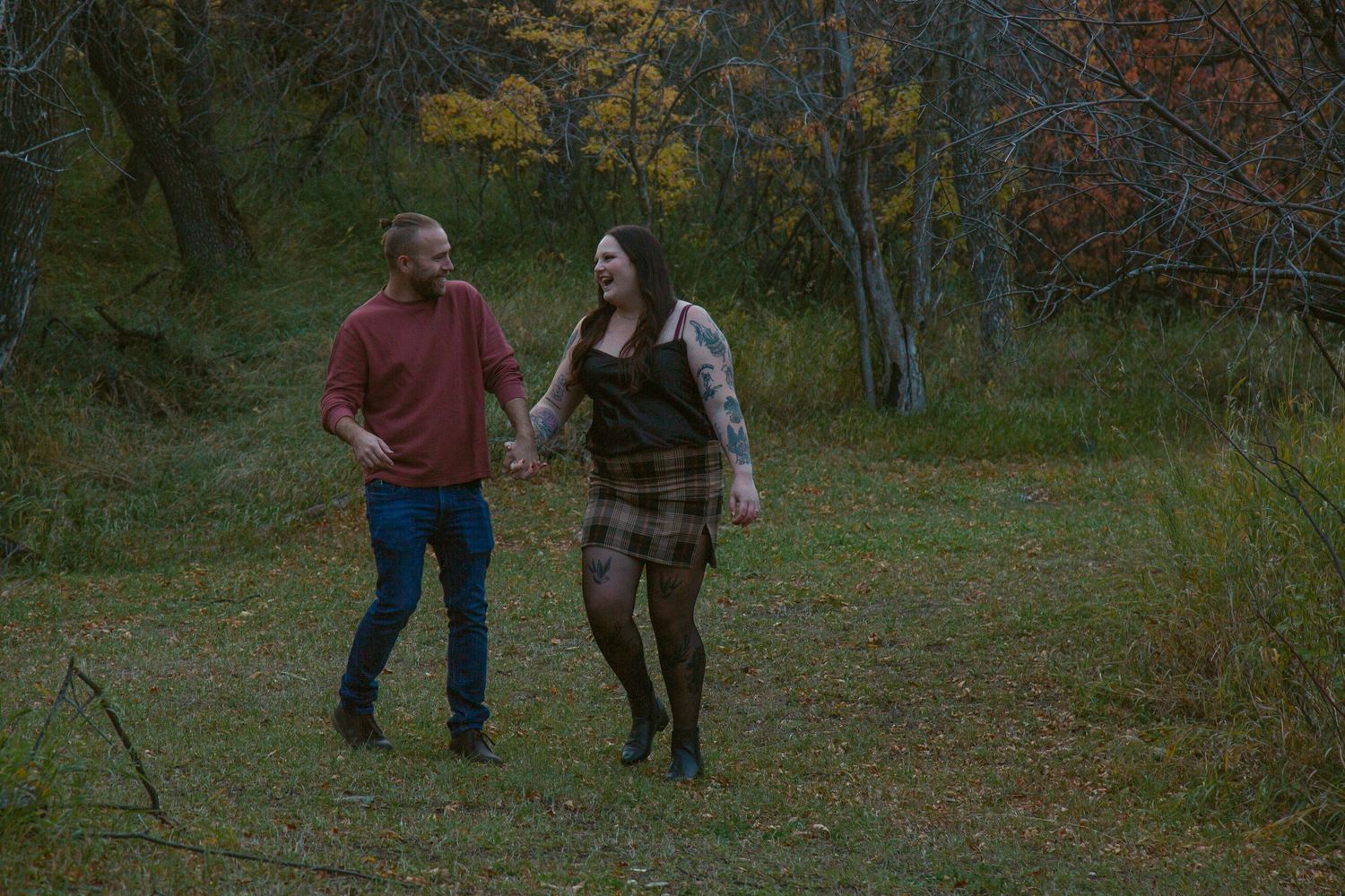 A couple walks hand in hand through an autumn forest trail.