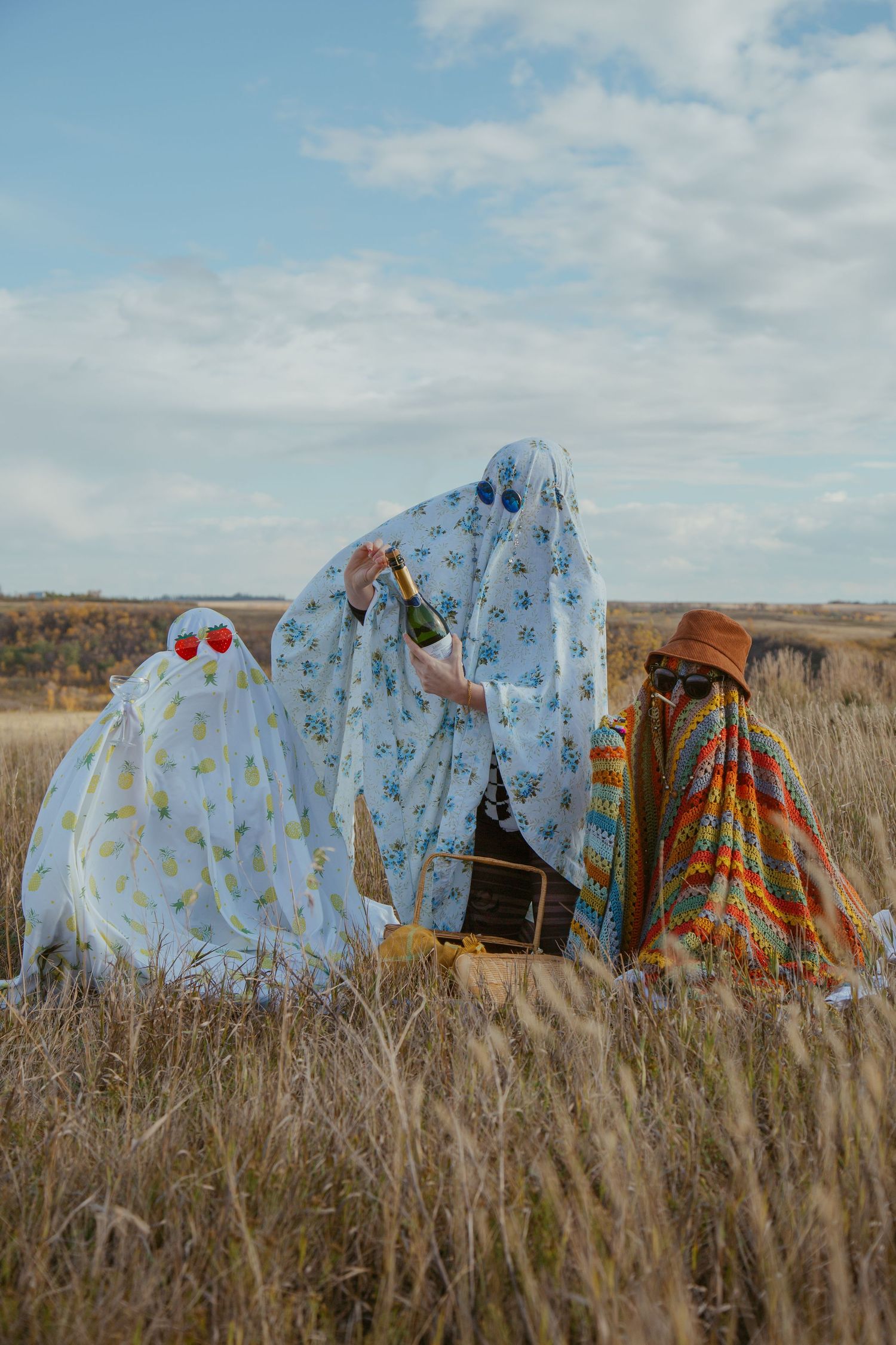 Colorful ghost costumes with polka dot patterns stand in a grassy field against a cloudy sky.