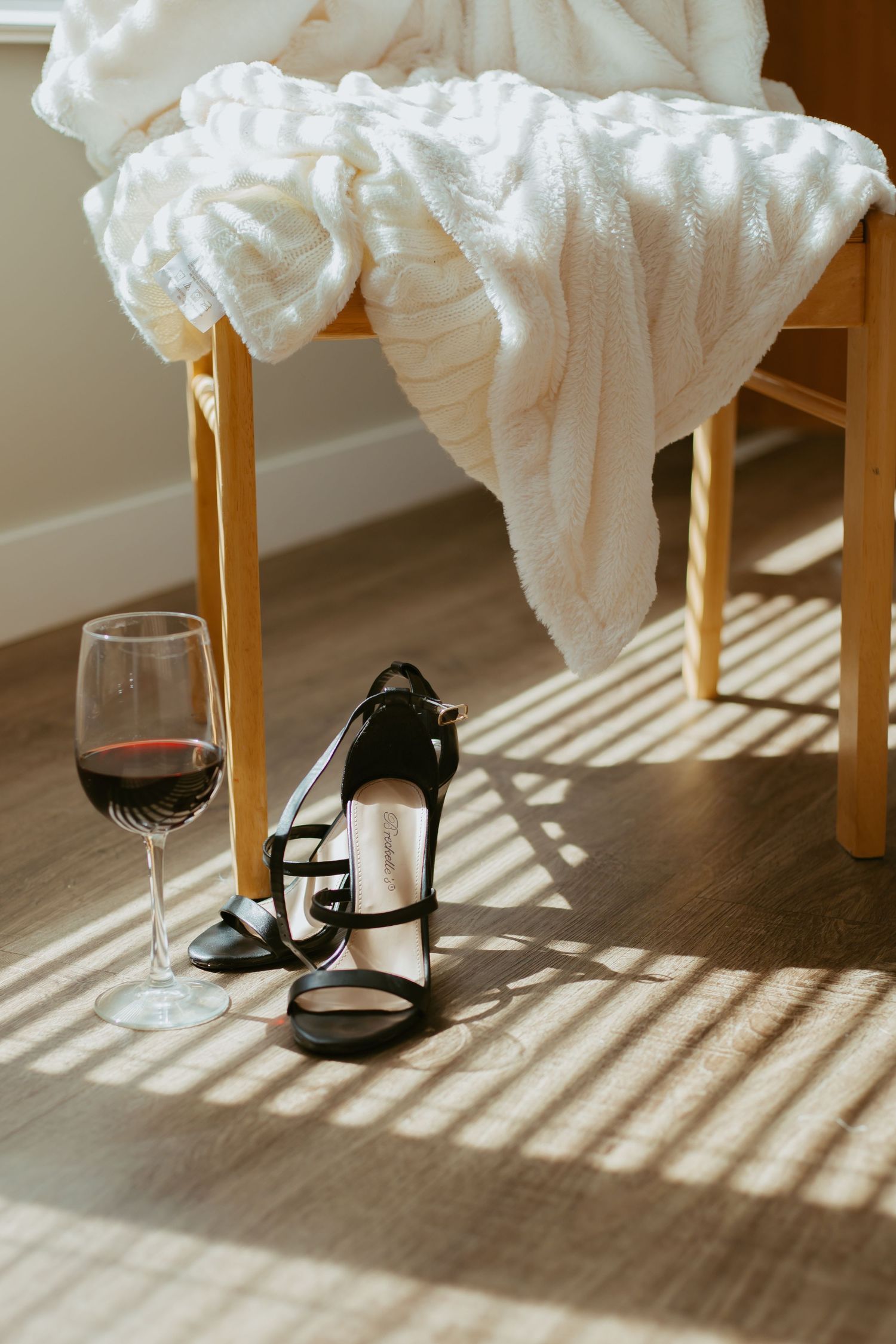 Elegant still life with strappy heels, wine glass, and white fabric in morning light.