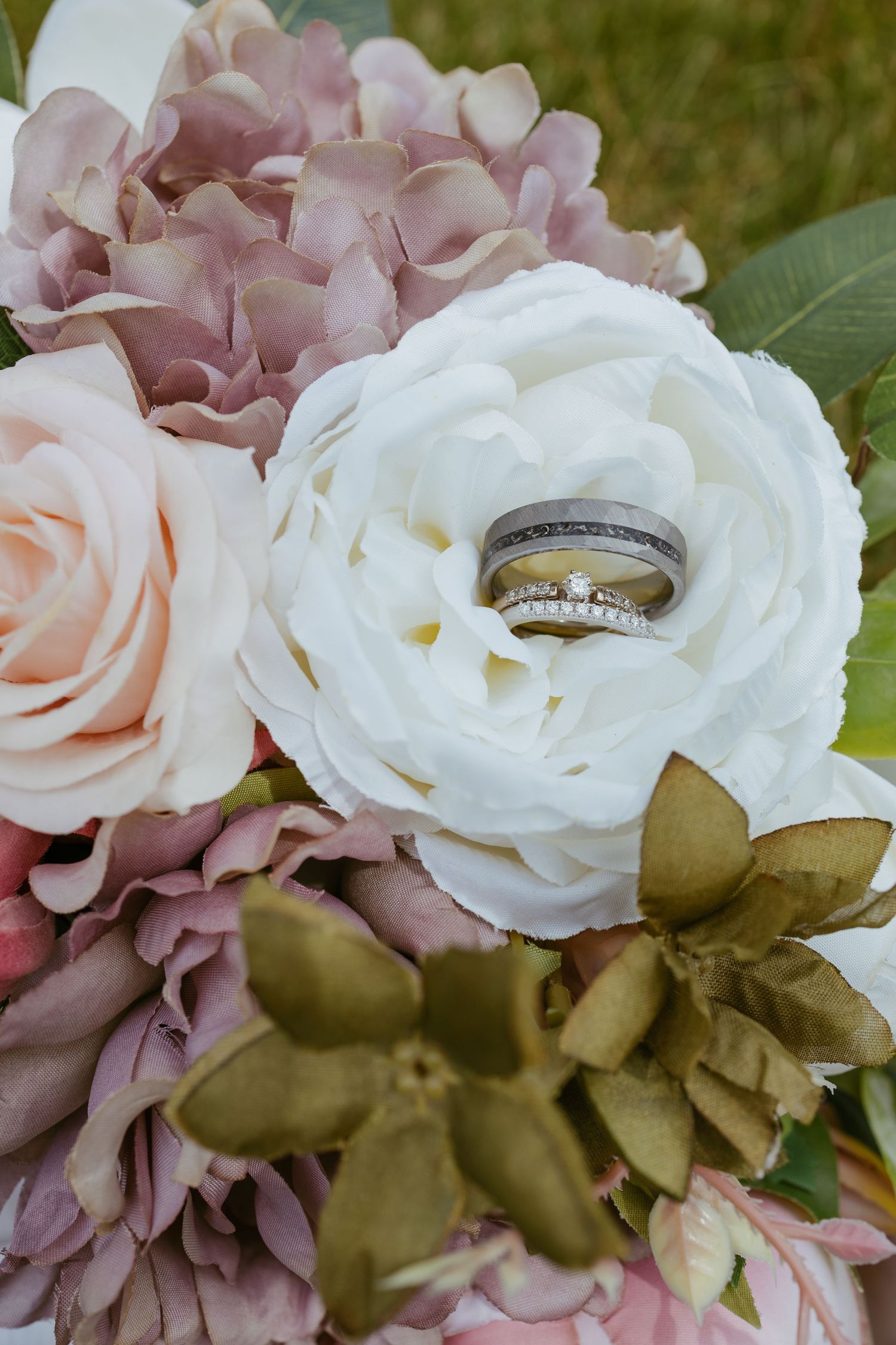 Wedding rings nestled among white and pink roses with green foliage.