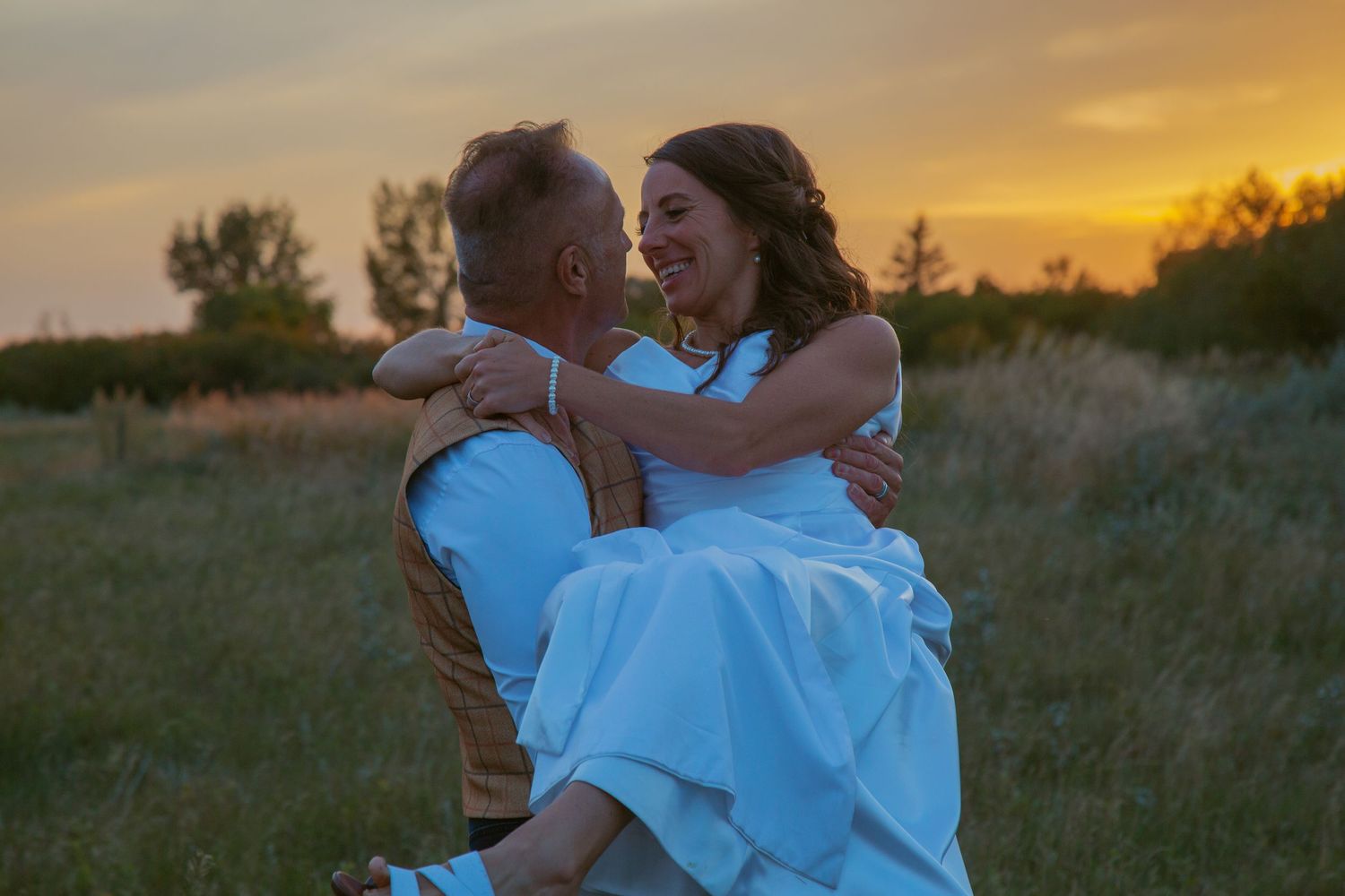Dancing couple twirls in an open field during a romantic sunset photoshoot.