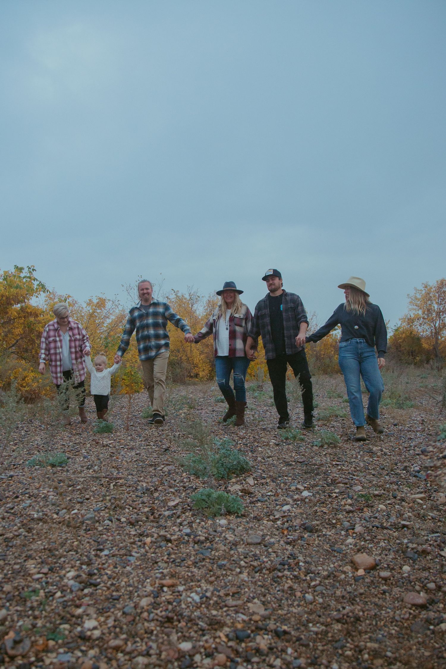 Group walking together on rocky terrain wearing casual western attire against autumn landscape.