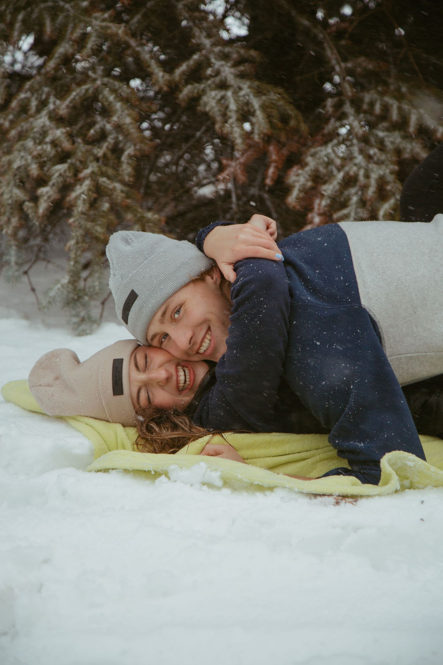 Couple cuddling together on blanket in snowy winter scene.
