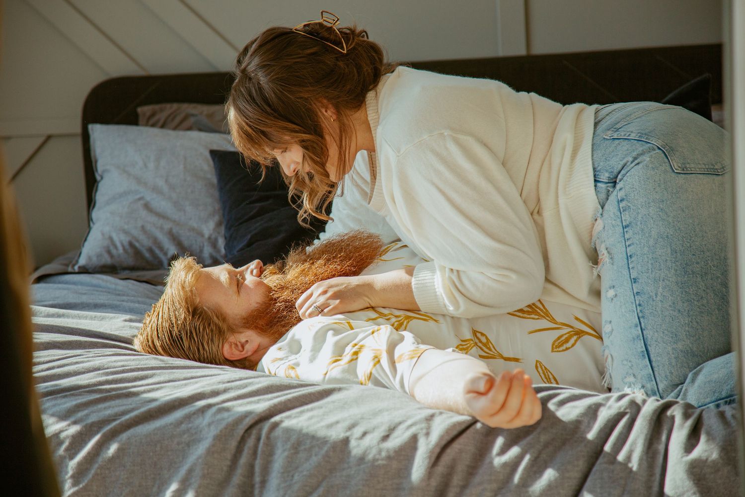 A tender moment shared between parent and child lying on white bedding in warm sunlight.