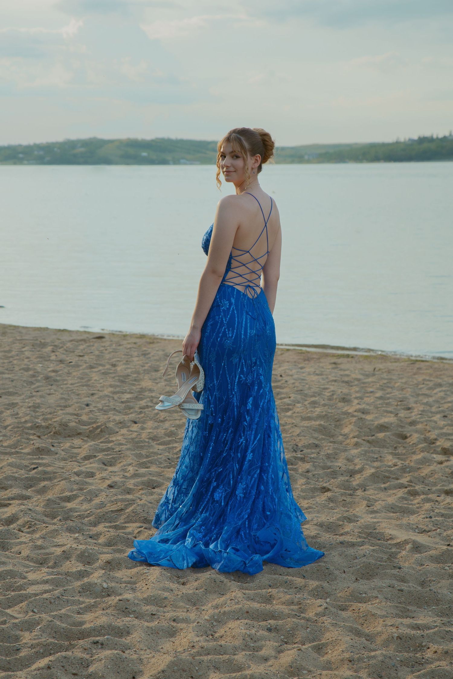Figure in flowing blue dress walking along sandy beach with water view.