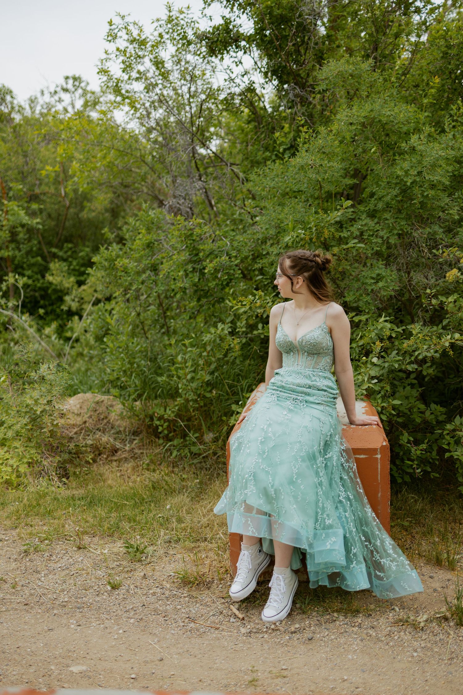 Person in mint green dress sits on vintage furniture outdoors among trees.