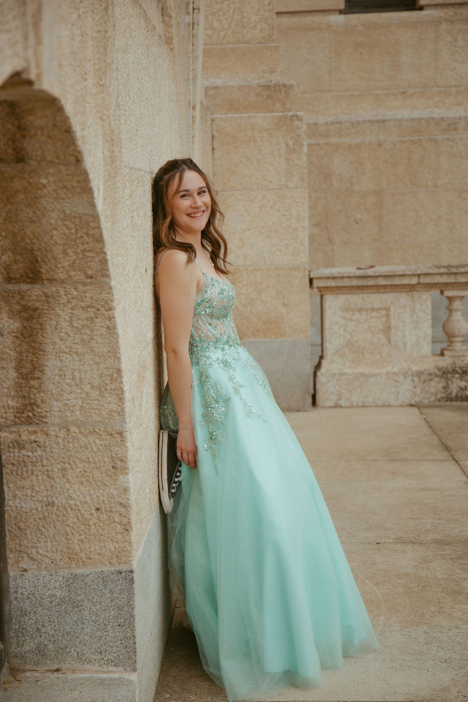 Person in a mint green formal gown poses against a stone wall.