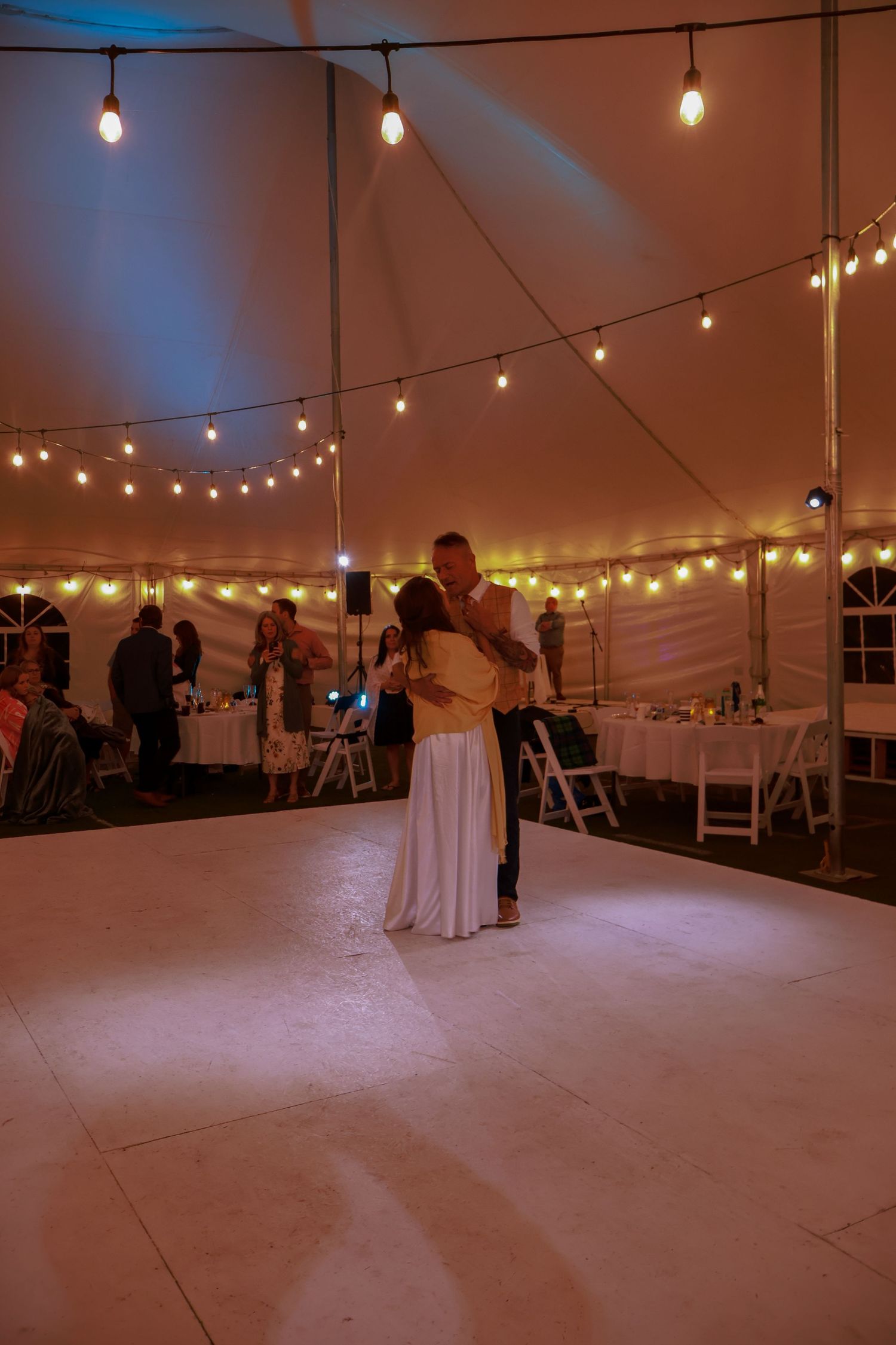 An empty white tent venue space illuminated by warm string lights creating an ambient atmosphere.