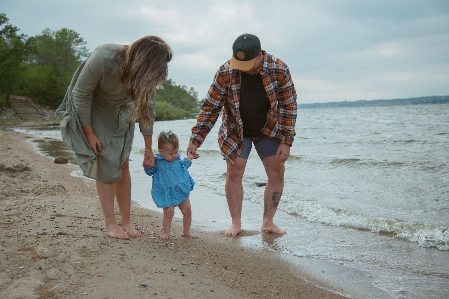 Family members walk along the shoreline of a beach with waves lapping at their feet.