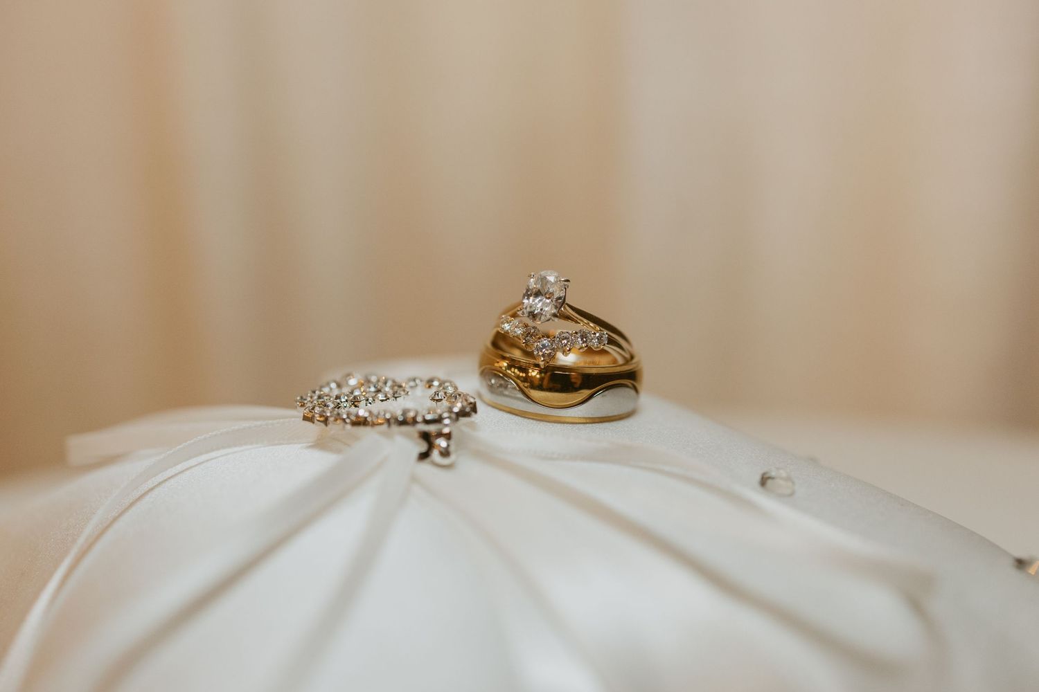 Wedding rings and jewelry displayed elegantly on white fabric with soft beige background.