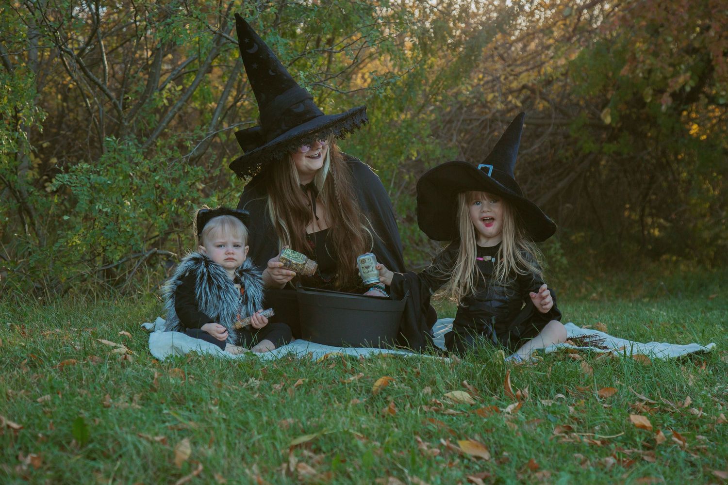 Halloween scene with witches and children gathered around a cauldron in autumn setting.
