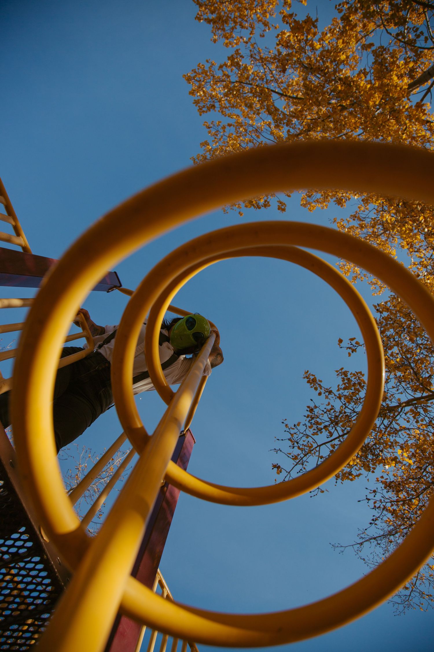 Yellow spiral playground equipment photographed against blue sky and autumn foliage.