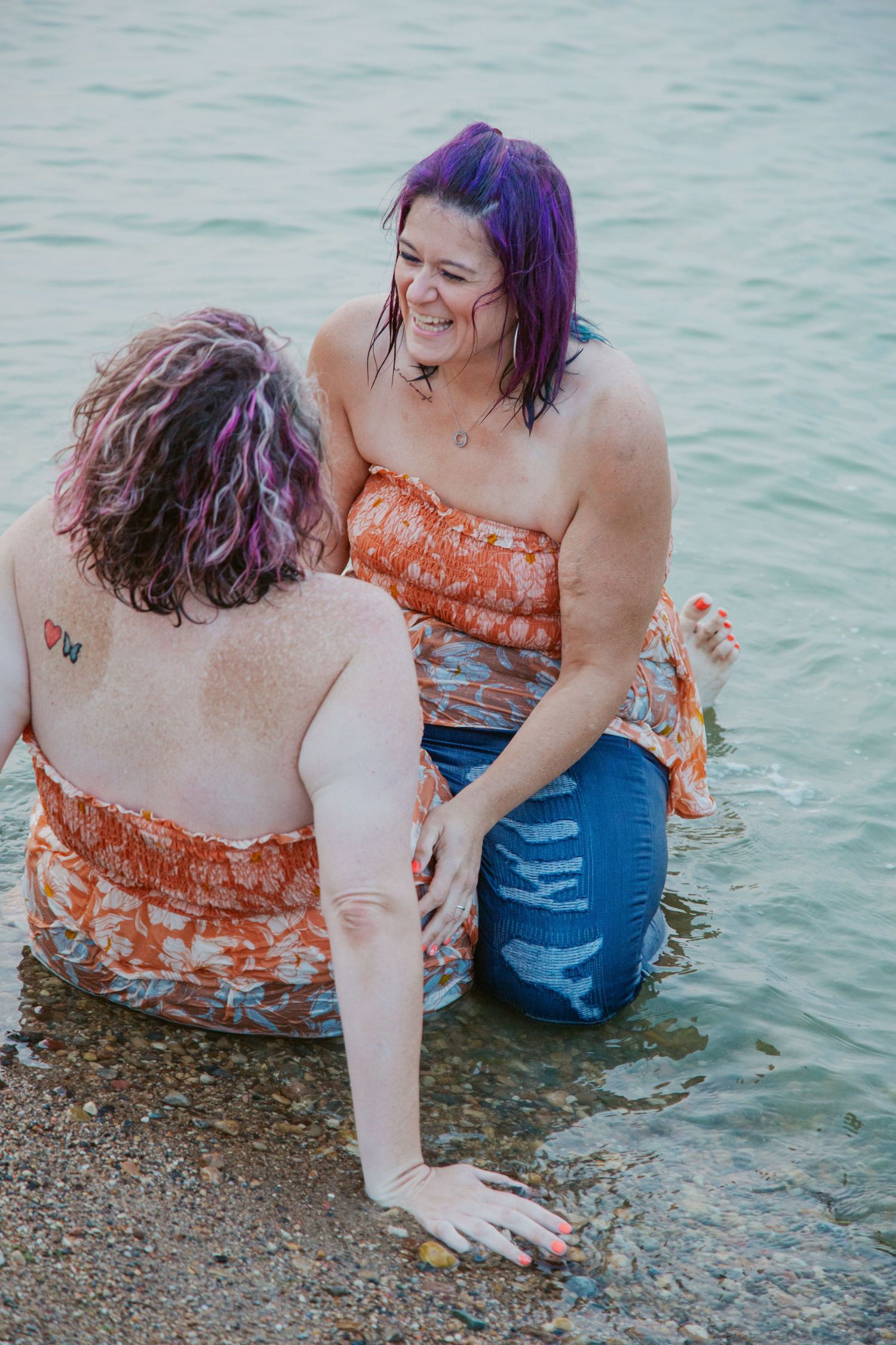 Friends enjoying a summer day while sitting in shallow water wearing orange and blue outfits.