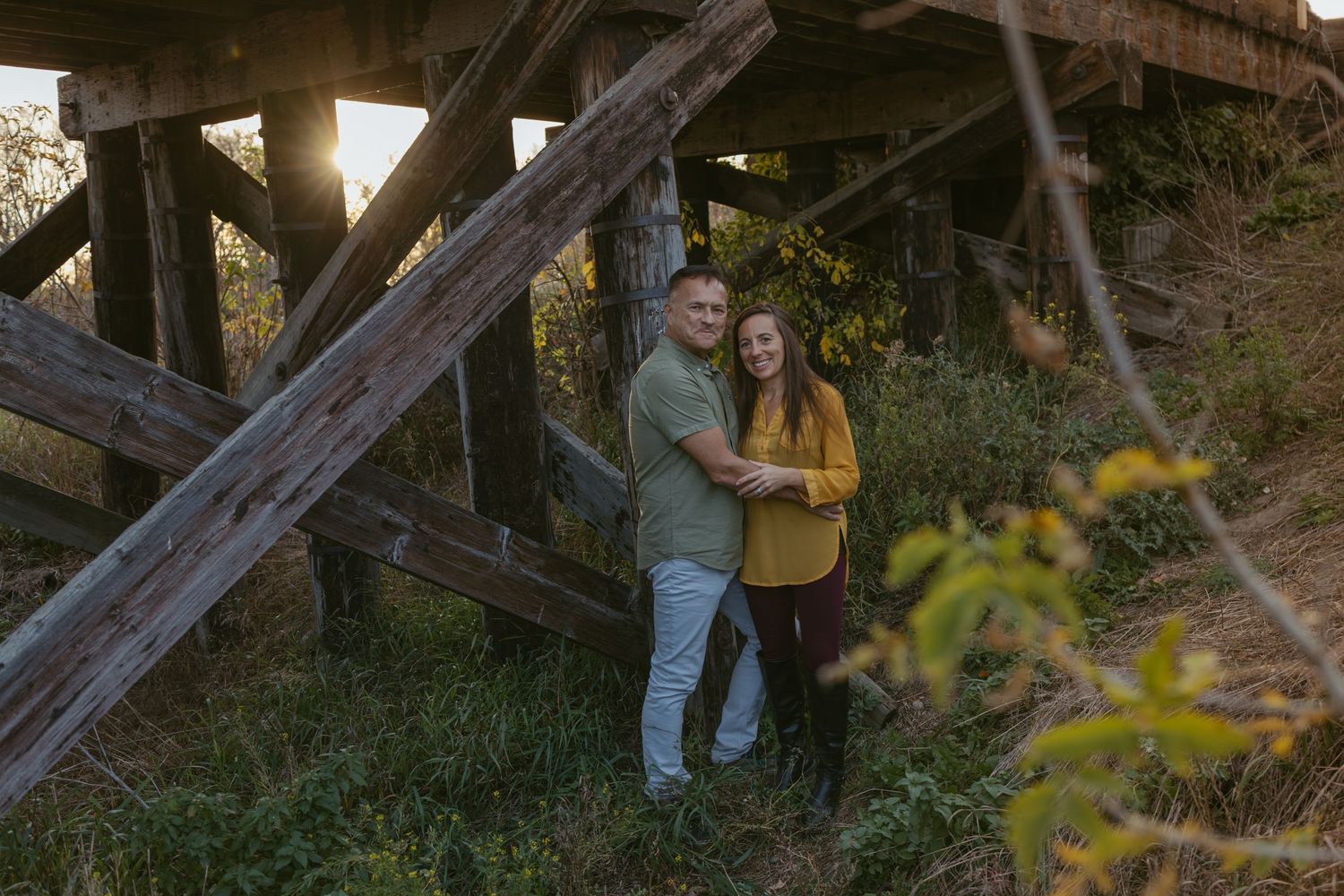A couple walks through a wooded area with sunlight filtering through the trees during golden hour.