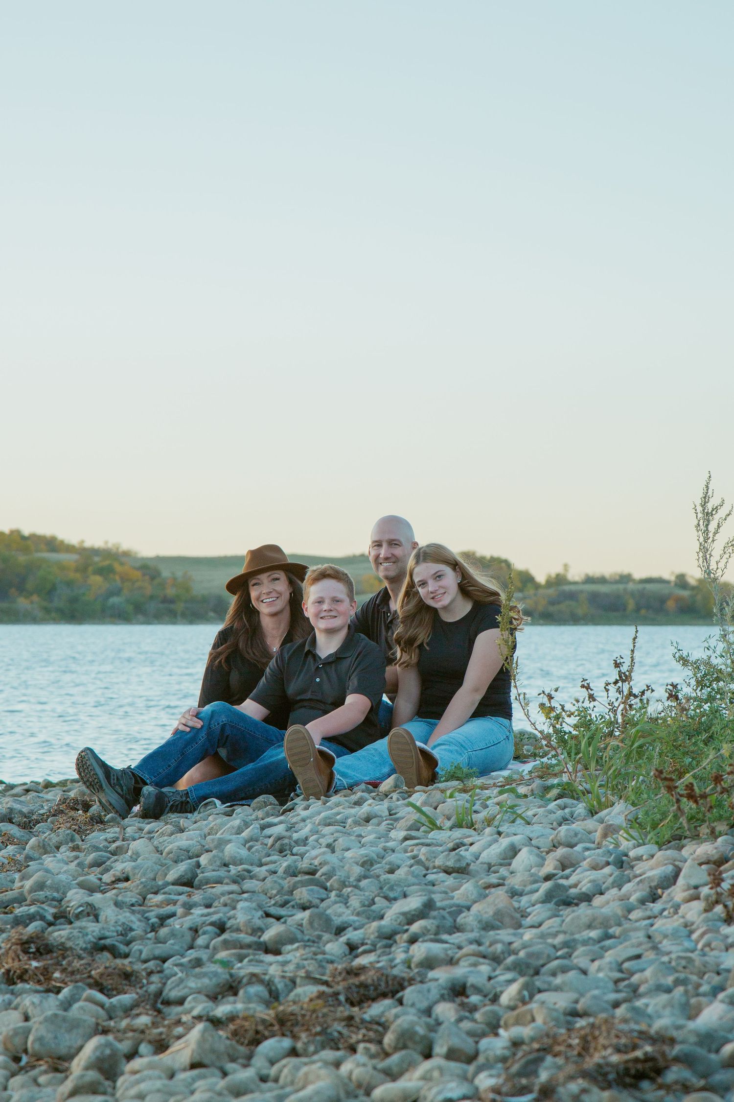 Group relaxing on rocky shoreline beside calm waters at dusk.