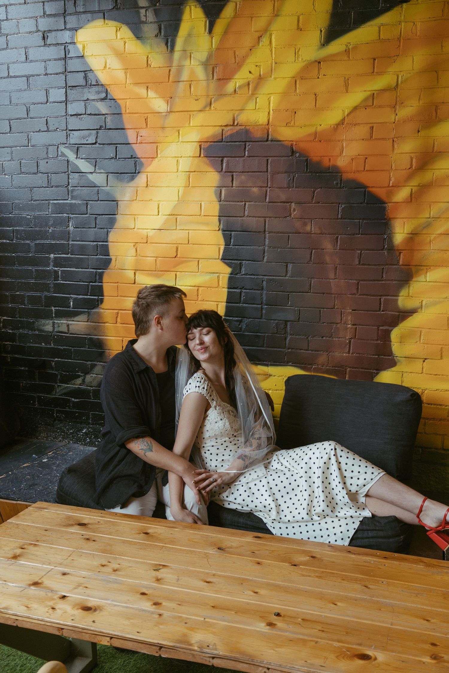 A couple relaxing on wooden benches against a colorful painted brick wall mural.