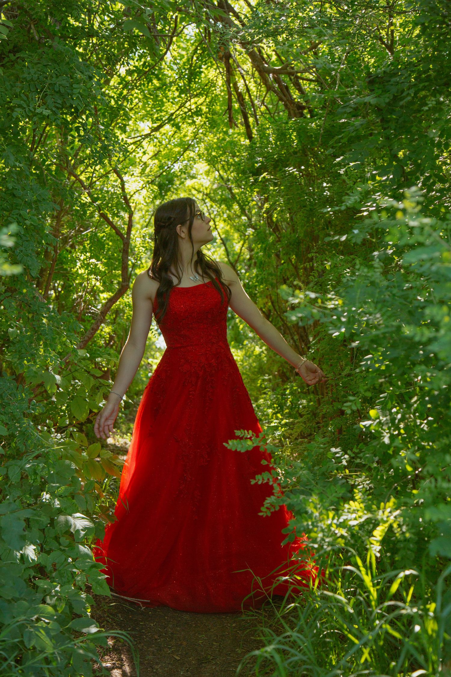 Flowing red dress contrasts with lush green garden foliage in dreamy outdoor setting.