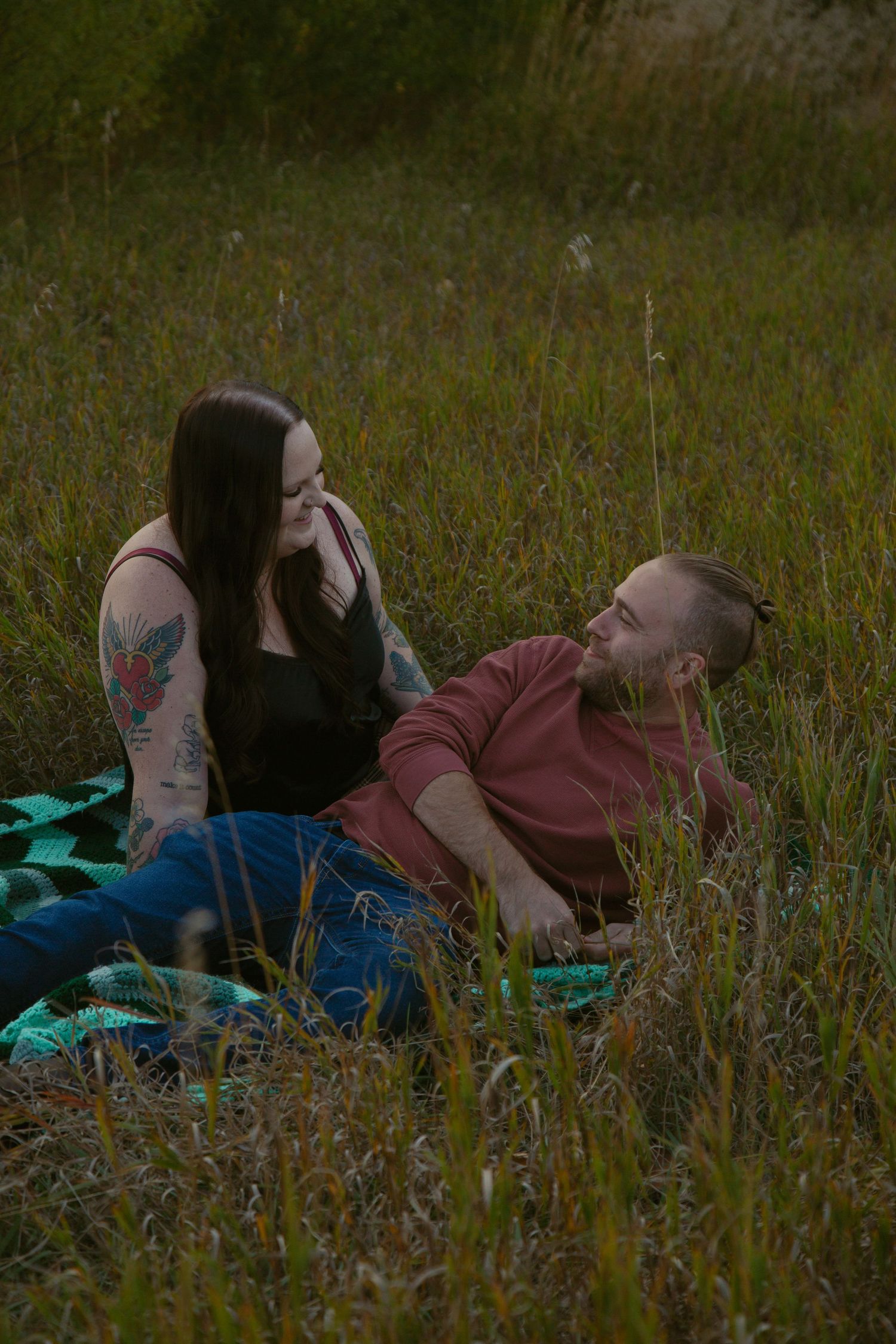 A couple shares an intimate moment while relaxing on a blanket in tall grass.