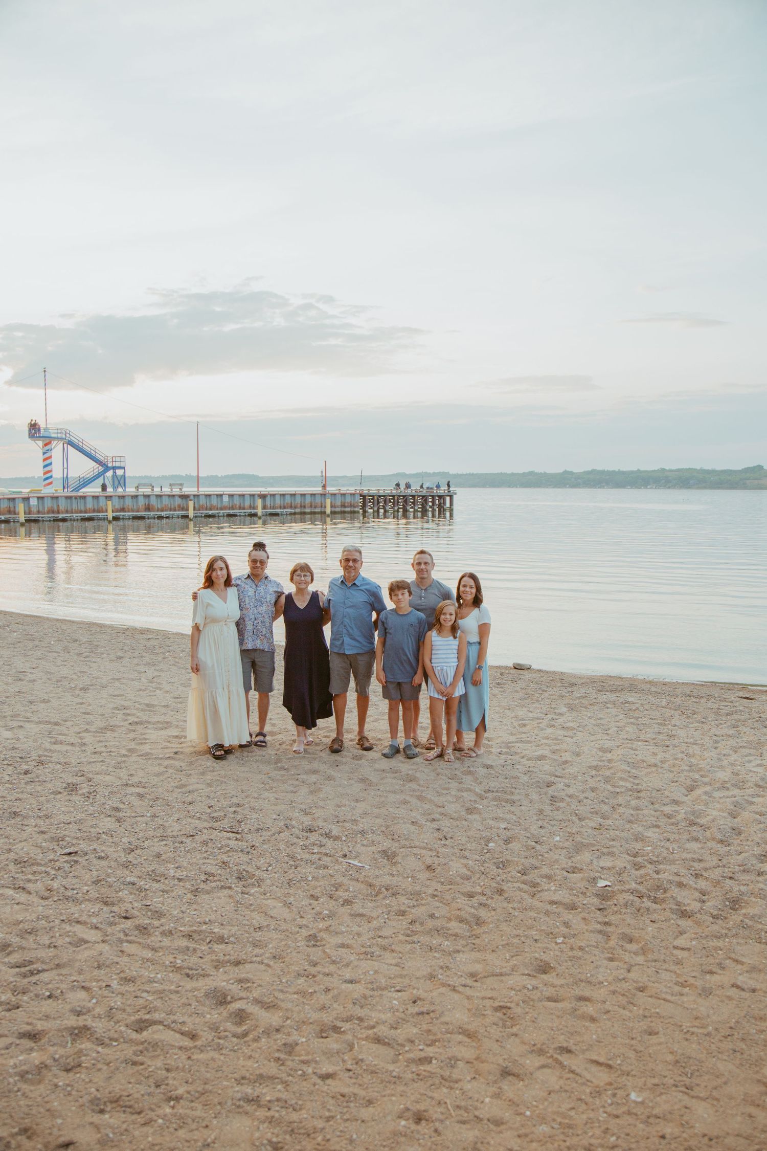 Small group poses together on sandy beach with pier and water in background at dusk.