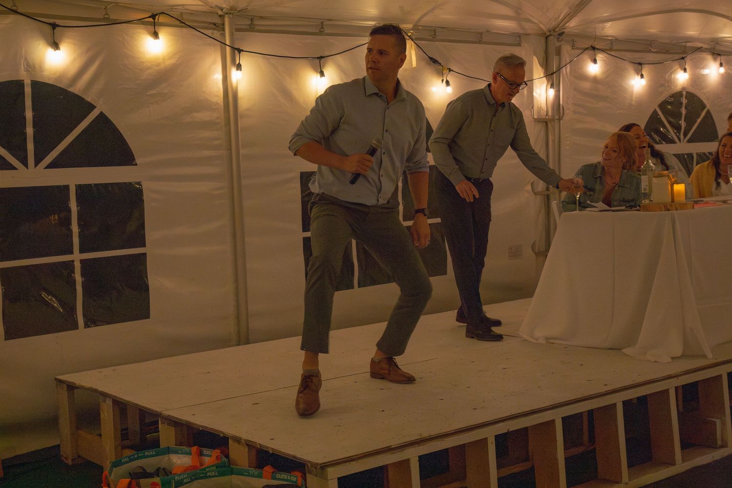 People dancing and celebrating under a white tent with string lights.