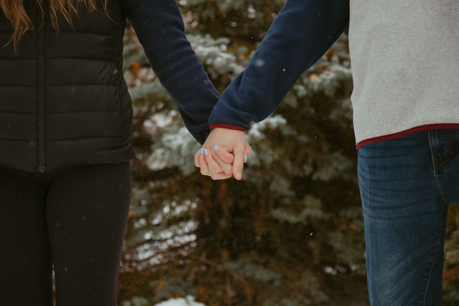 Close-up shot of two people holding hands against a blurred winter background.