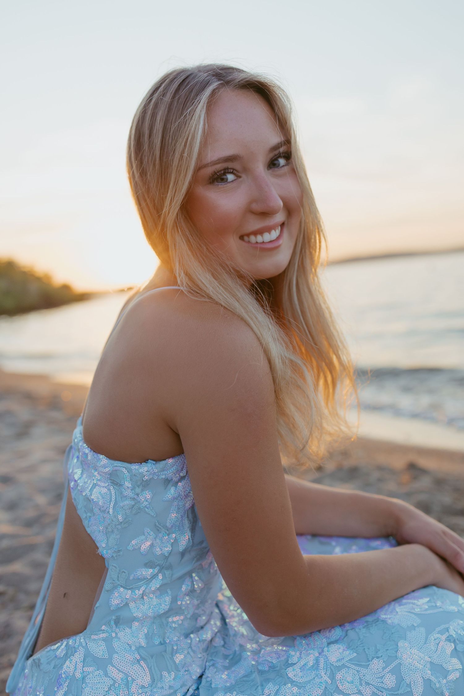 A person in a strapless blue dress poses on the beach at golden hour.