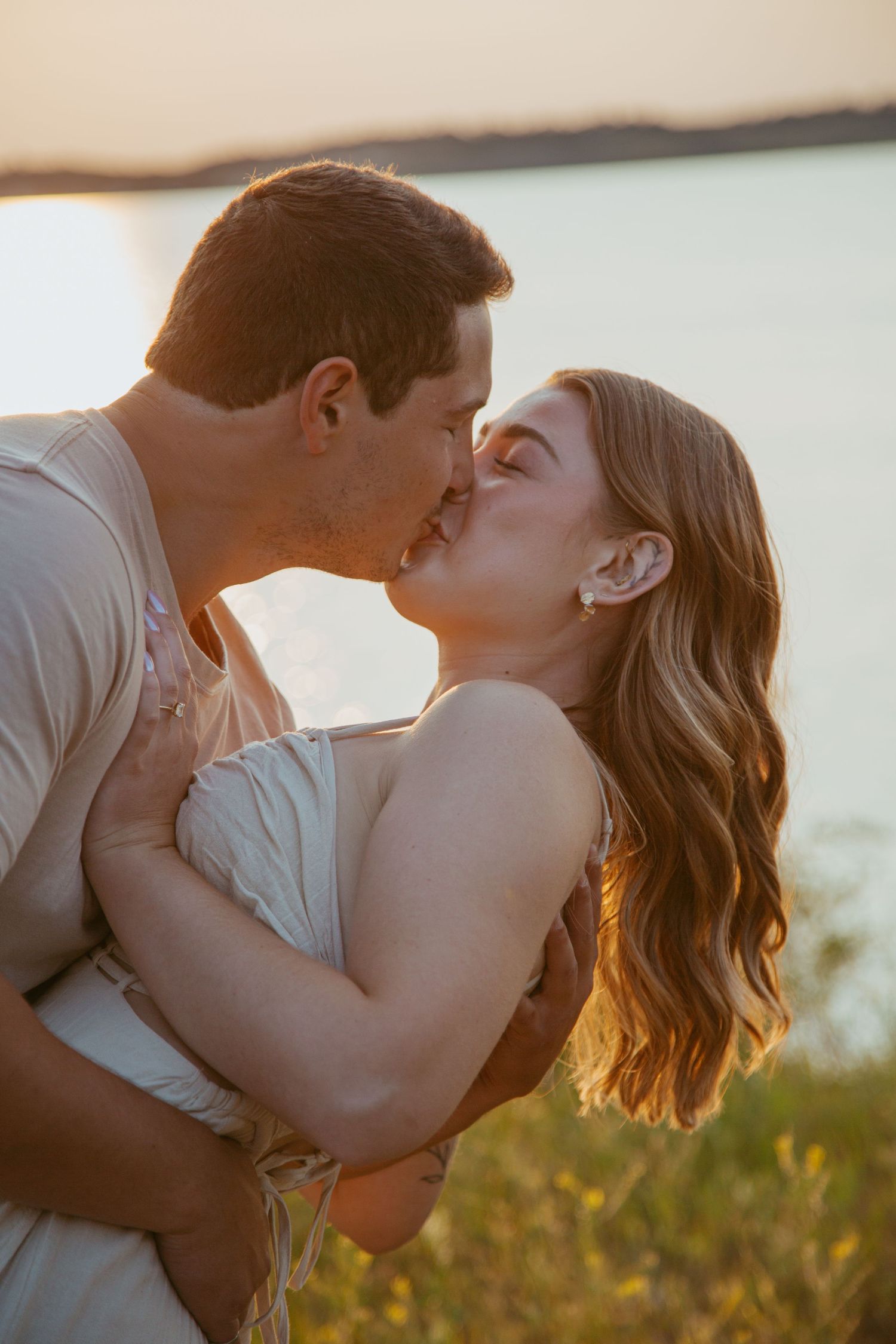 A romantic couple embraces during golden hour by the water.