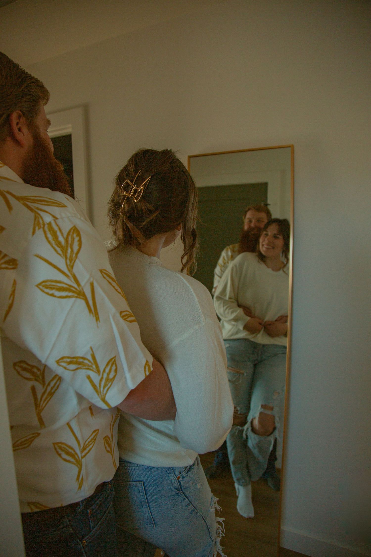 Couple looking at their reflection in mirror while standing in hallway.