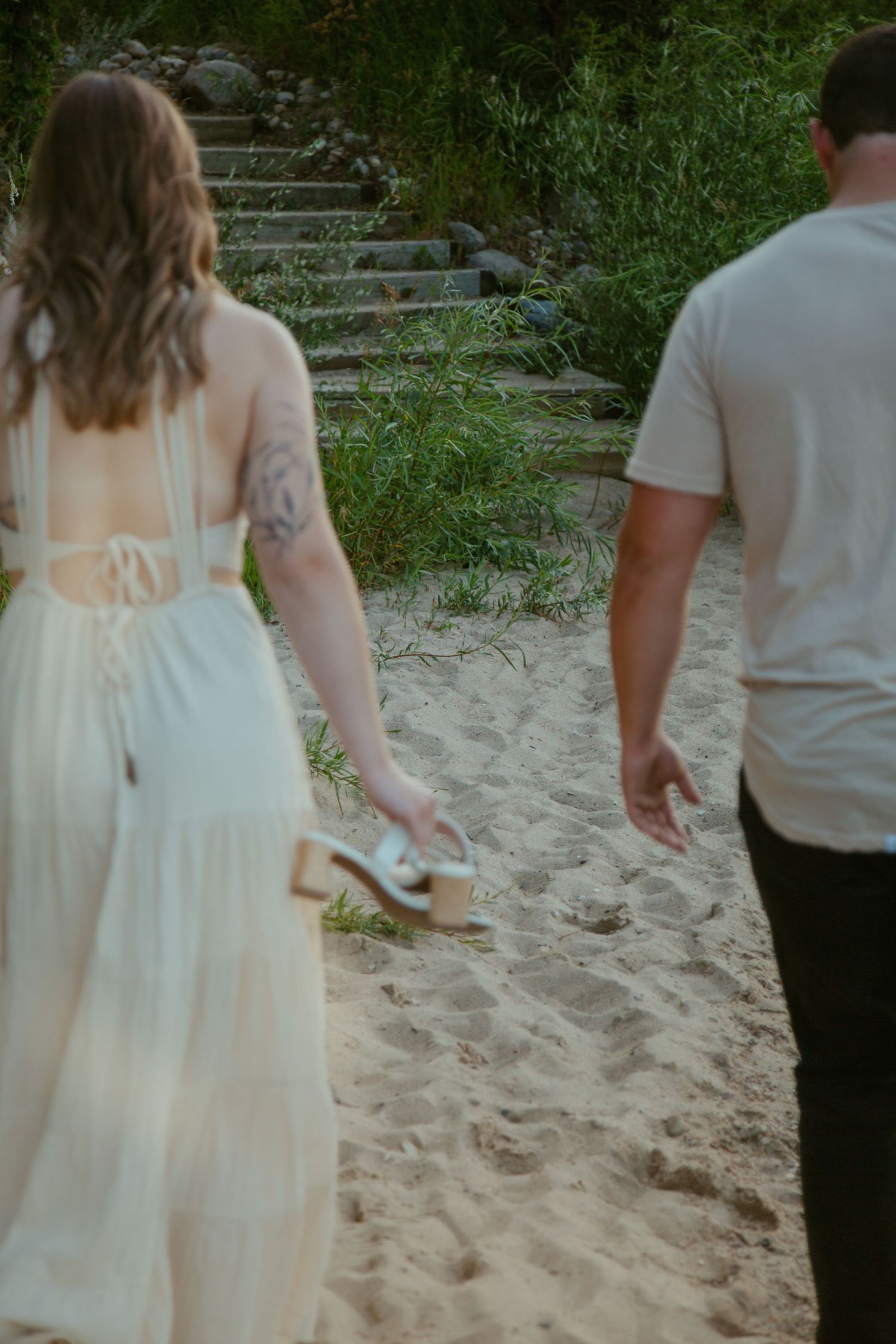 A couple climbs stone steps on a sandy beach path surrounded by greenery.
