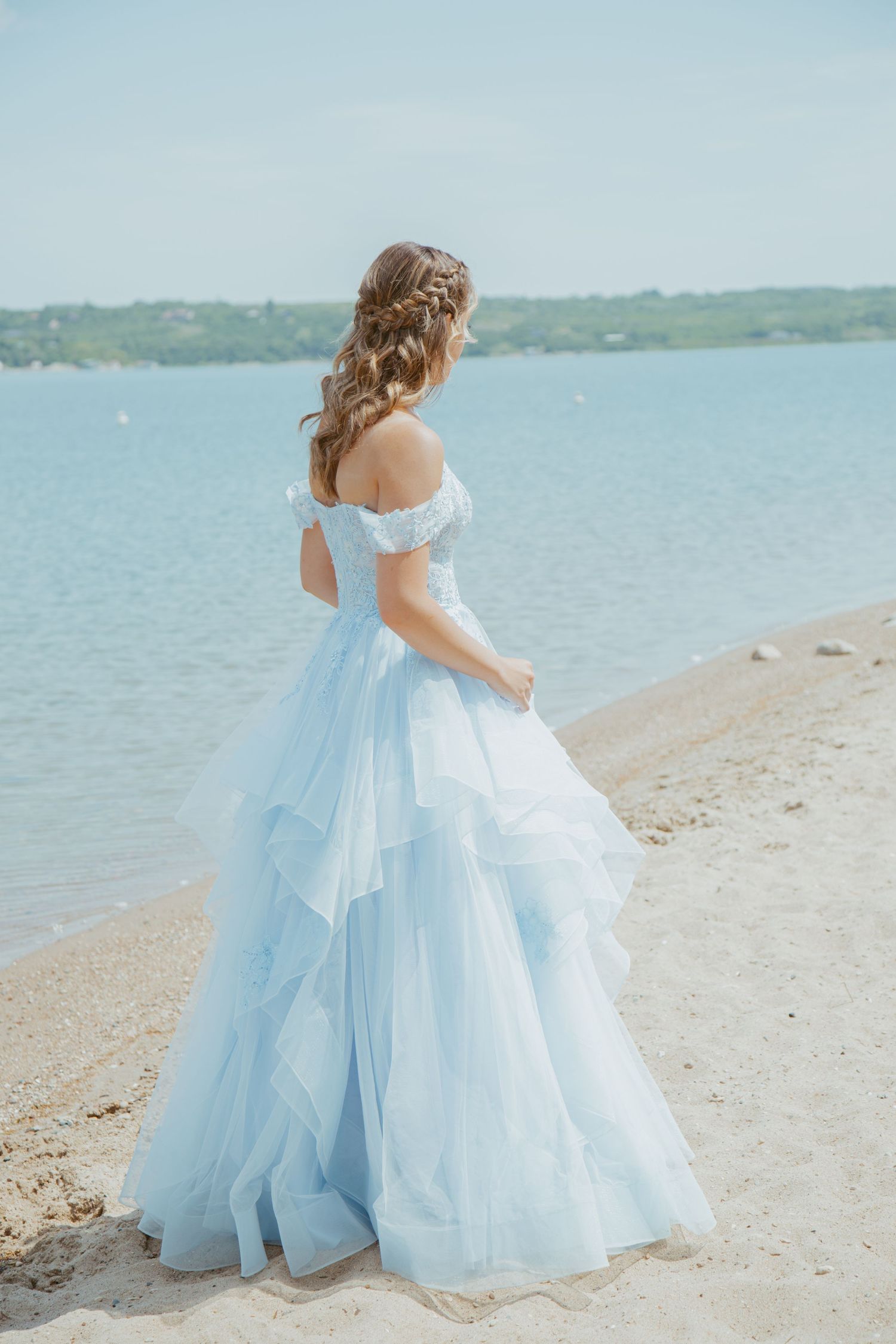 Two elegant ballgowns in light blue and white flow gracefully along a sandy beach with water in the background.