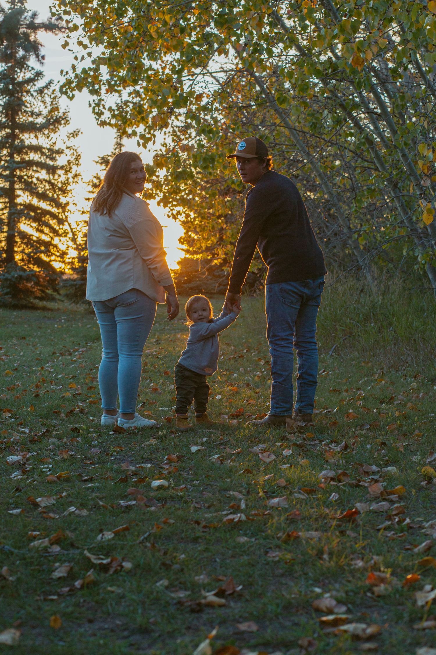Family walking together through fallen autumn leaves at sunset in a park.