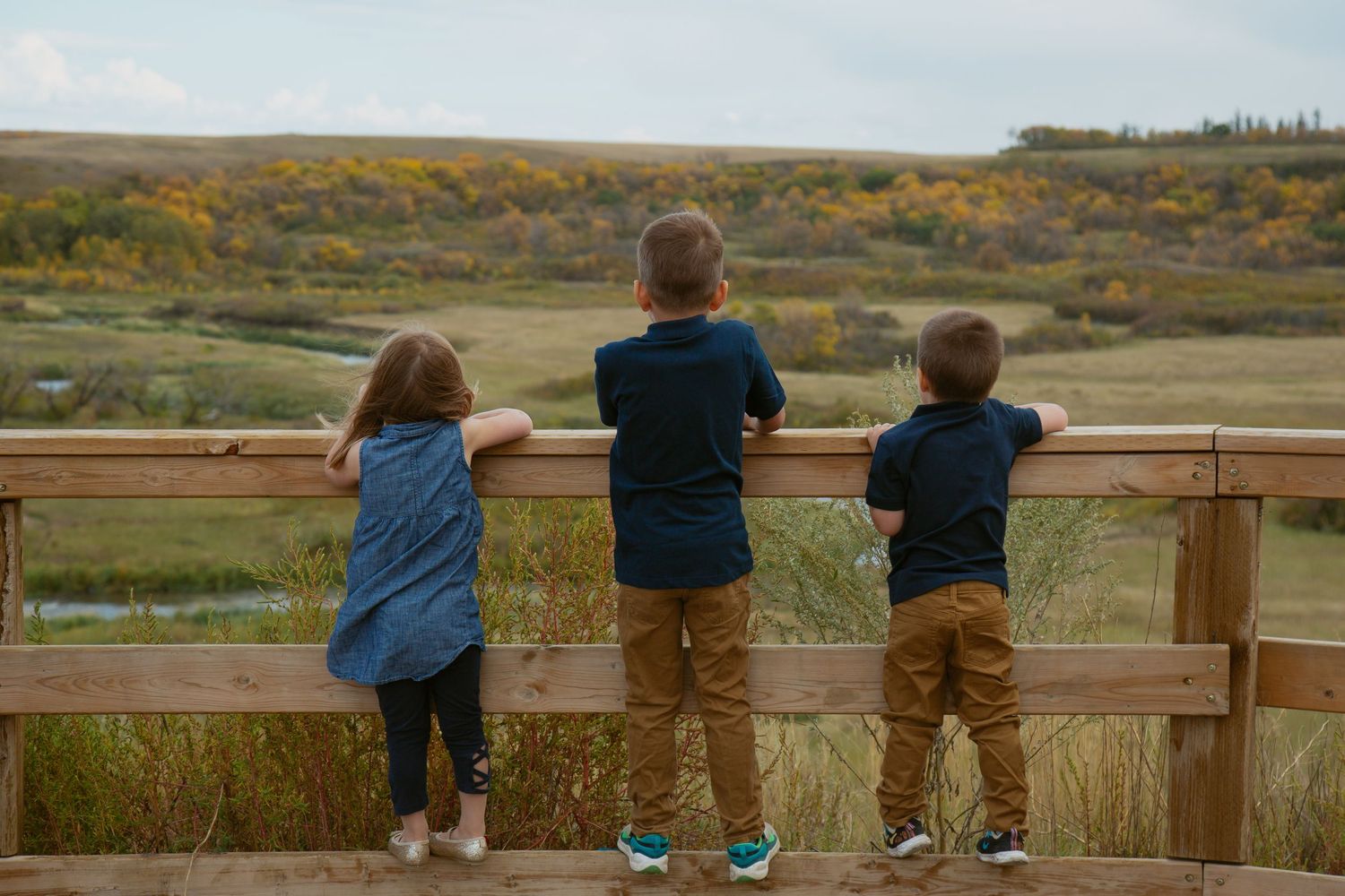 Group sitting on wooden railing overlooking autumn landscape at sunset.