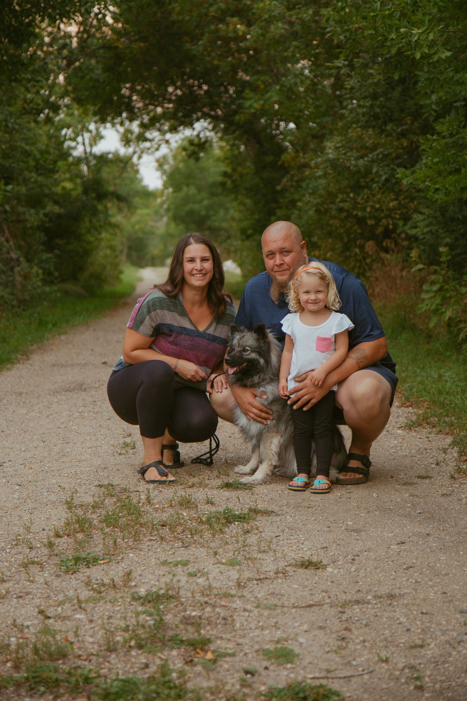Family and dog relaxing together on dirt path surrounded by green foliage.