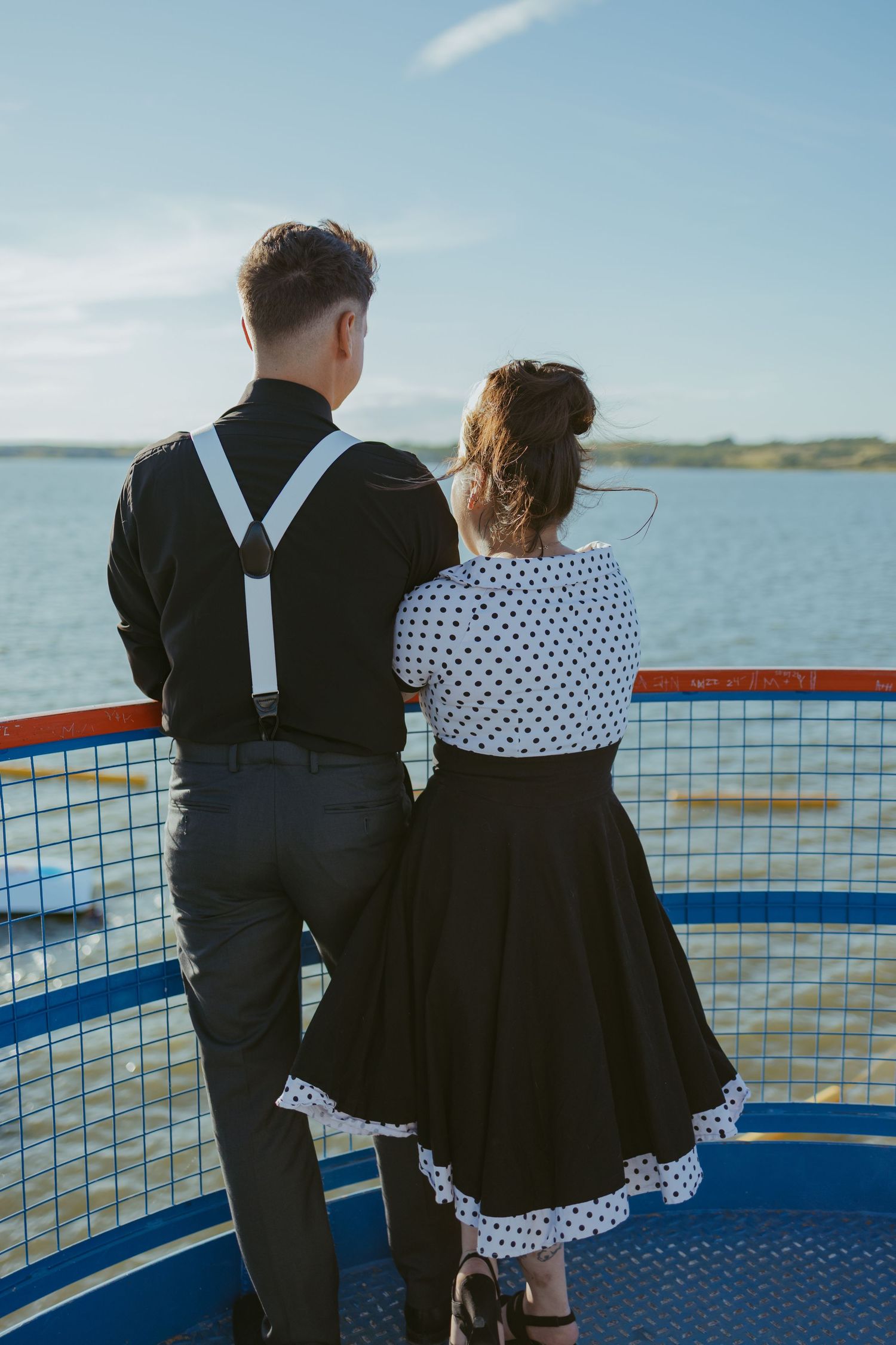 Couple in vintage attire looking out over water from a ferry deck.