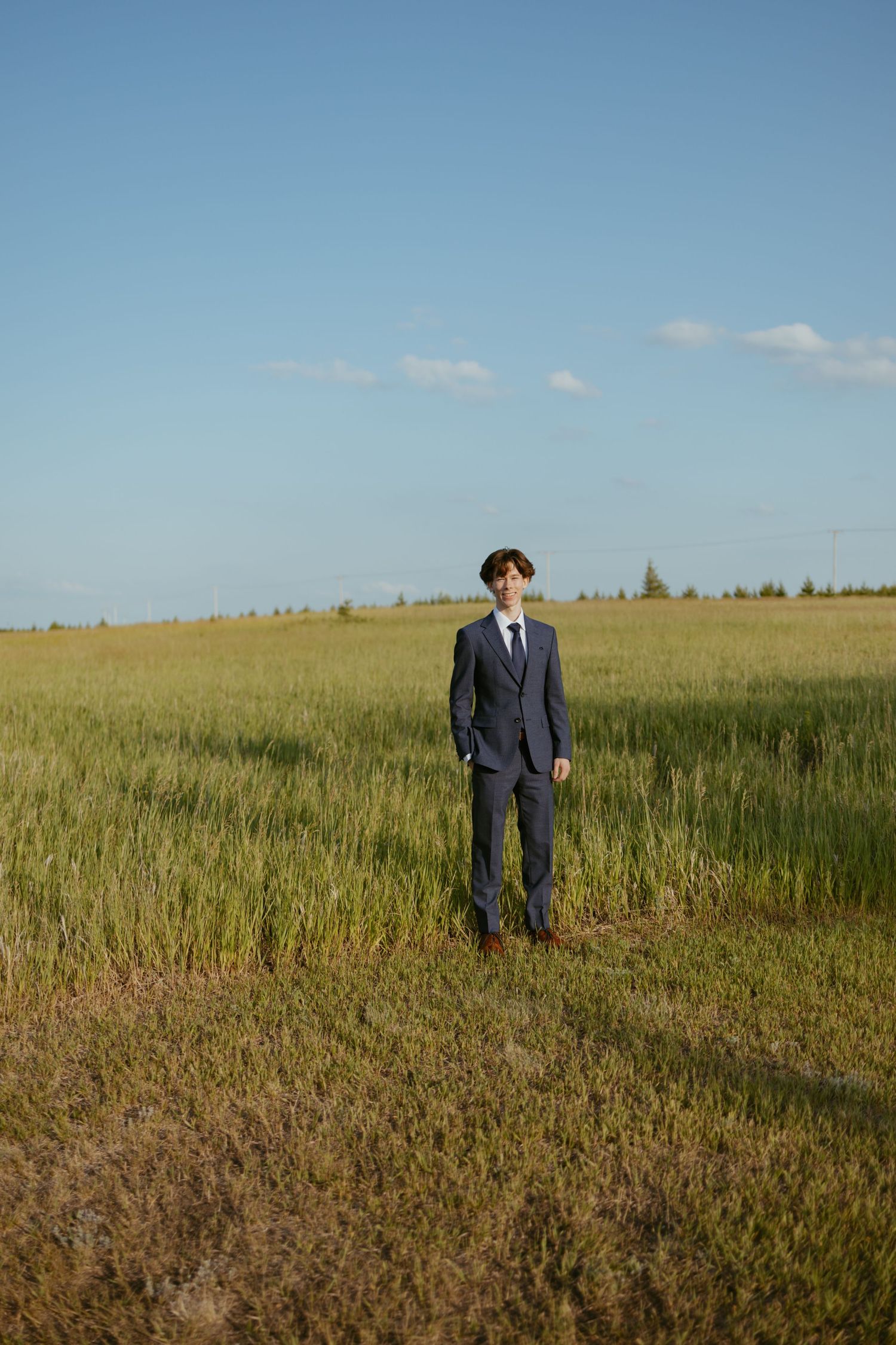 Figure in dark suit stands alone in vast golden field under blue sky.